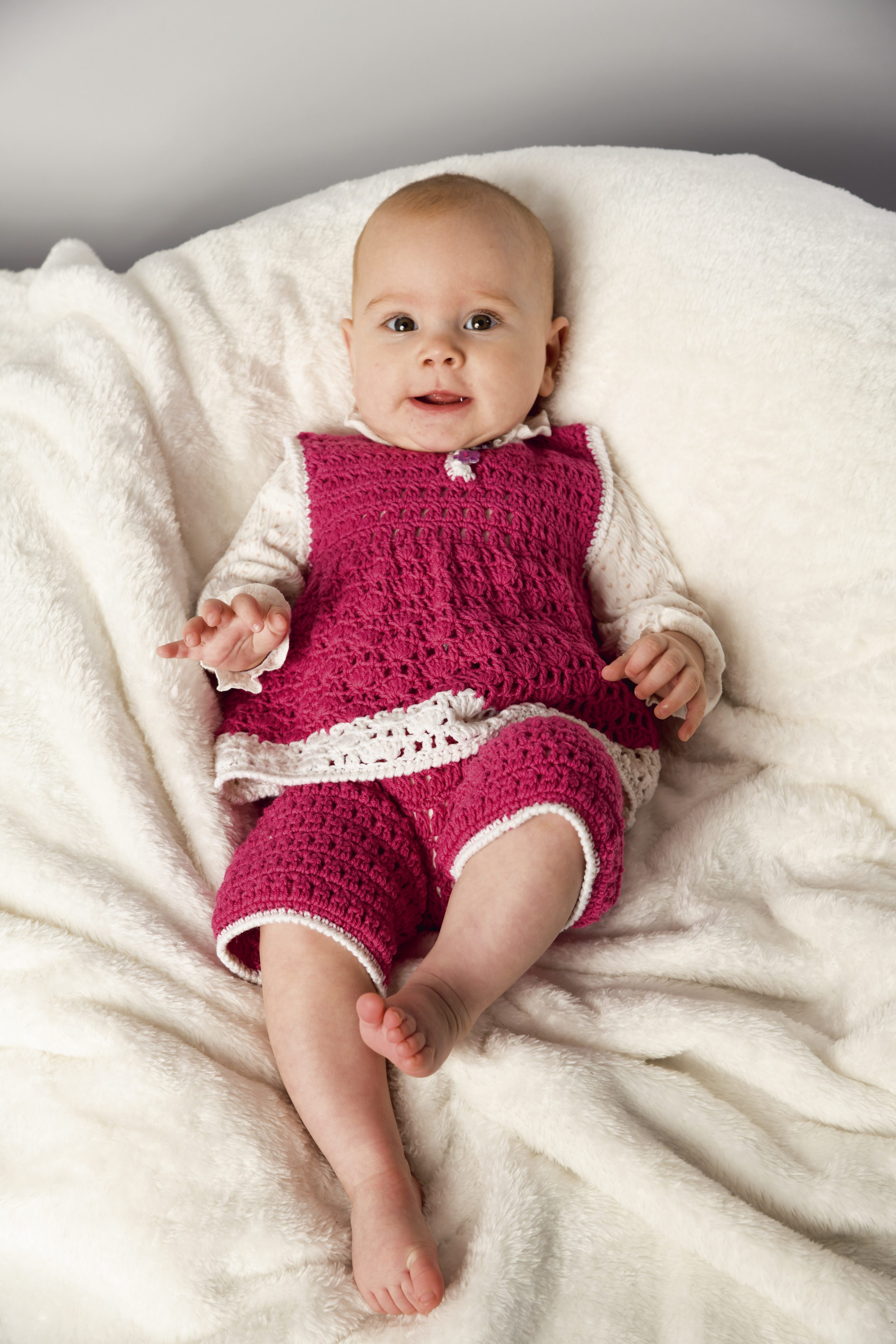 Handgemachter Strampler in kräftigem Pink, mit Häkelmuster und weißem Rand, modischer Schnitt. Perfekt für Babys.