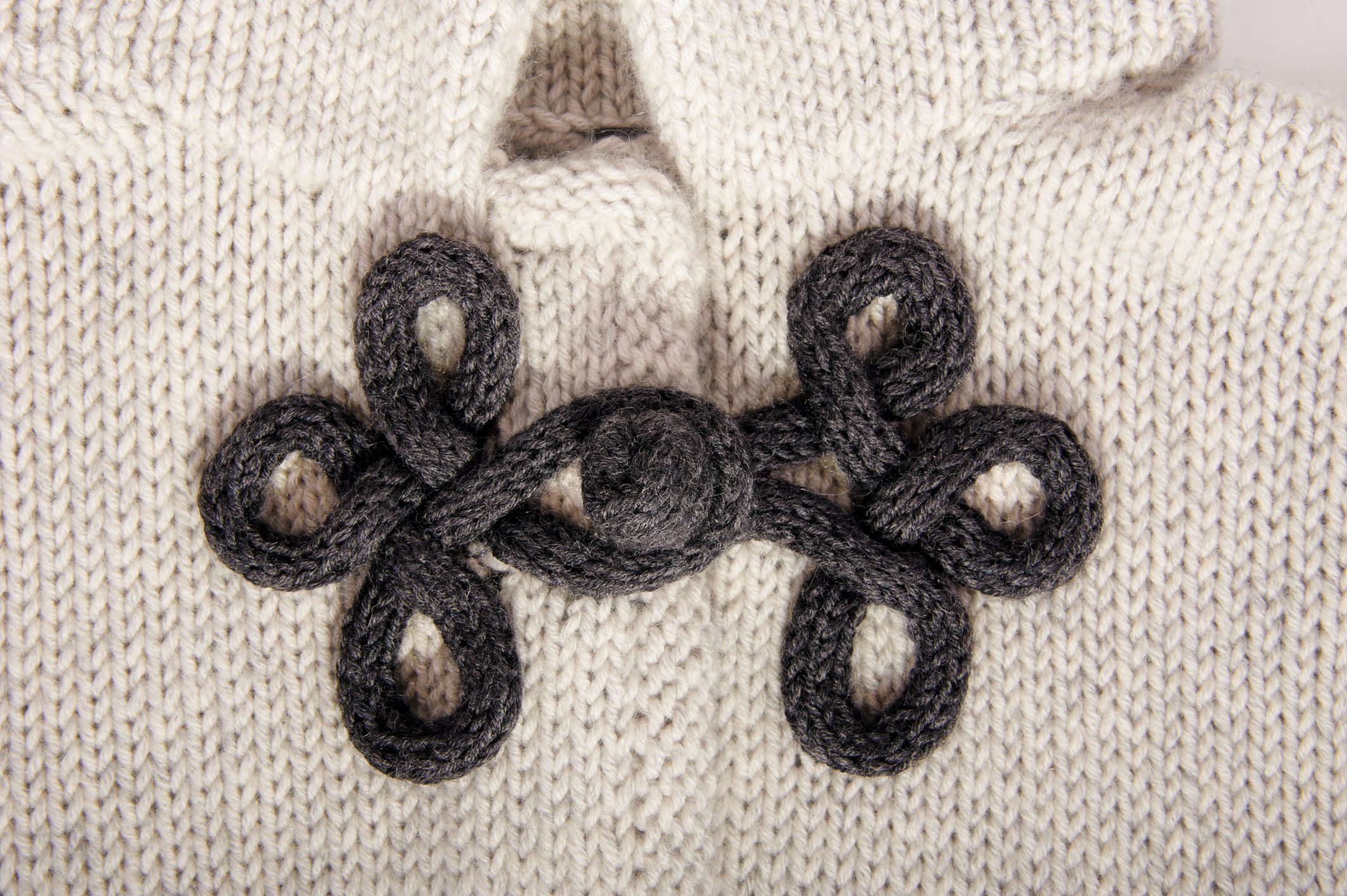 Cremefarbener Pullover mit handgemachter, schwarzer, verschlungener Verzierung. Modisch und detailreich.