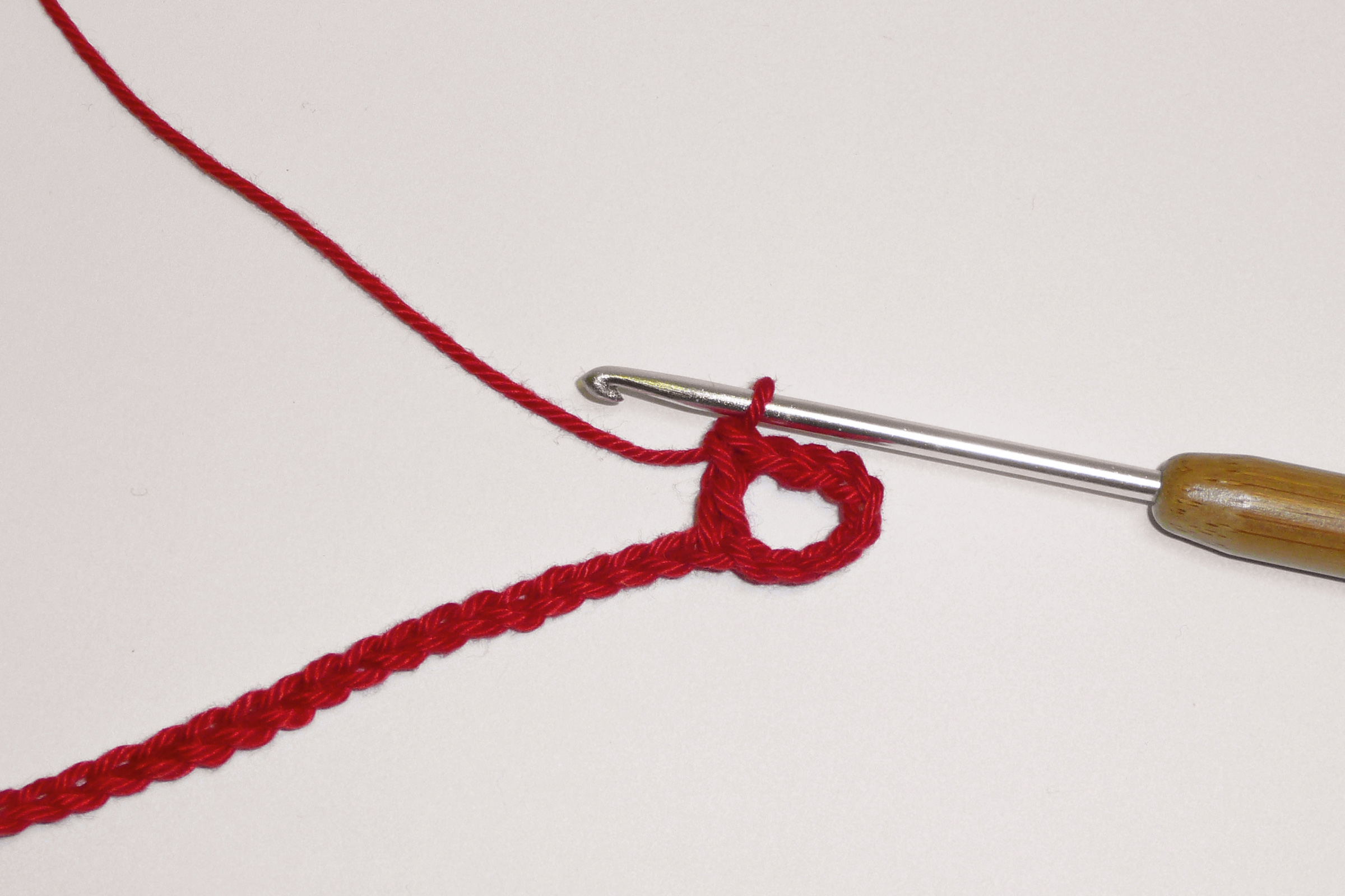 Rote Häkelarbeit mit Häkelnadel; handgemacht, selbstgemacht, kreativ; beginnt mit Schlaufenmuster.