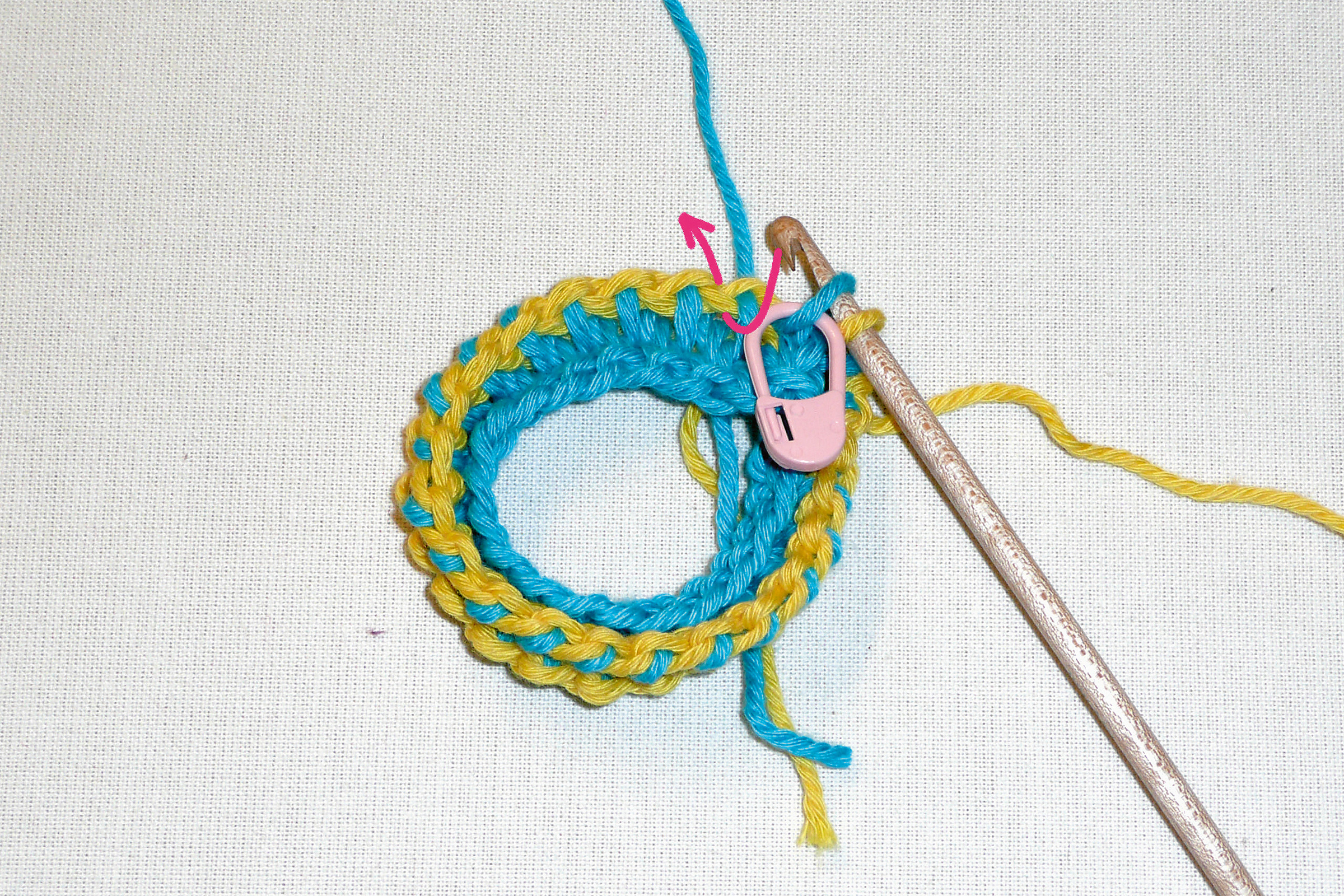 Handgemacht: Runde gehäkelte Struktur in Blau und Gelb, mit rosa Markierung. Lebendig und modisch.