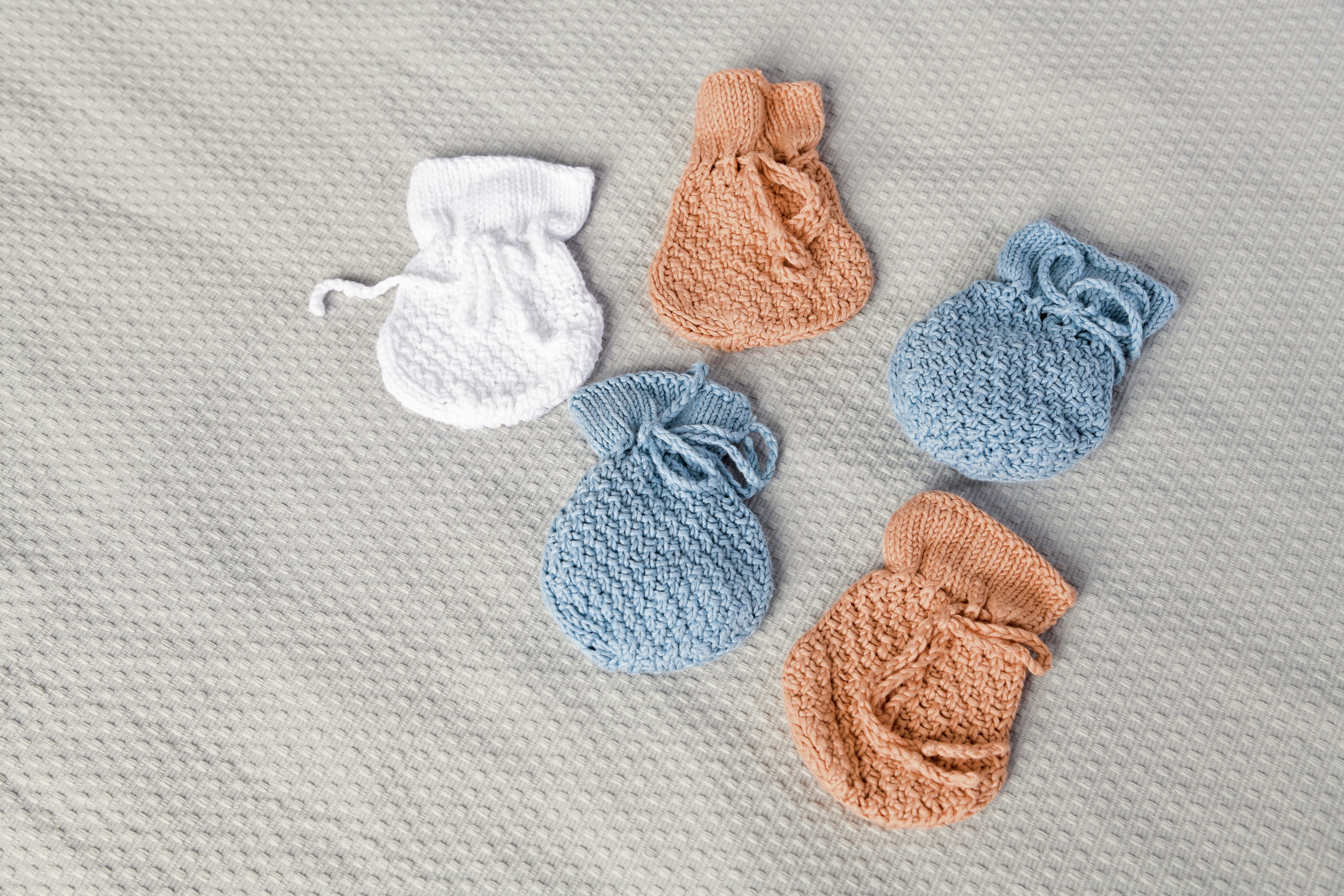 Selbstgemachte, gestrickte Babyfäustlinge in Blau, Weiß und Orange; weiches Muster, handarbeit.