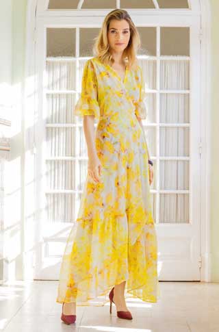 Langes, gelb-geblümtes Kleid mit V-Ausschnitt, transparenten Ärmeln; fließender Stoff, modisch und elegant.