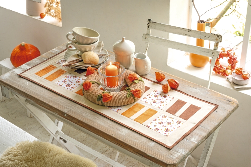 Modischer Tischläufer mit warmen Farben und floralen Mustern, handgemachter Kranz mit Herbstakzenten.
