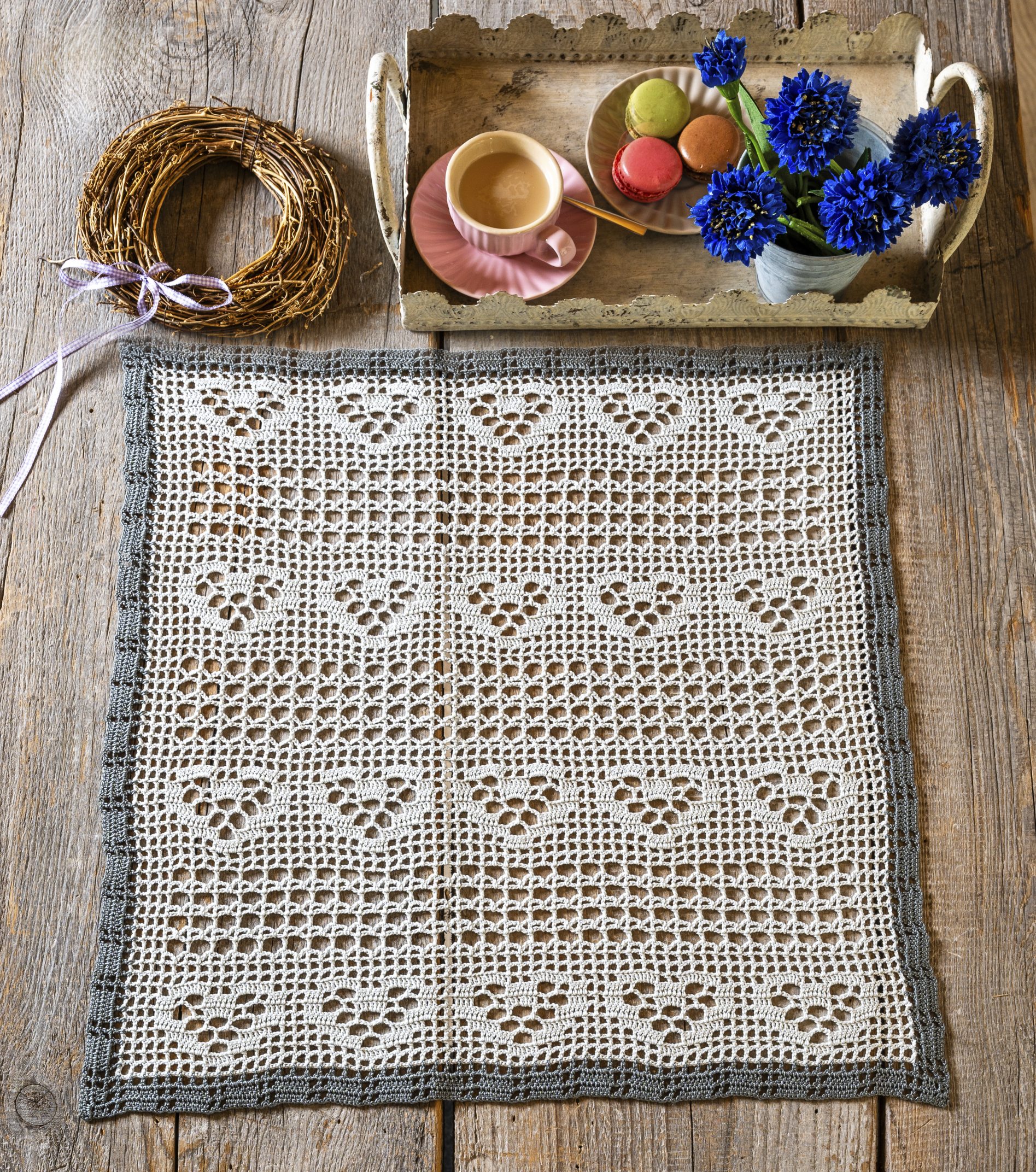 Handgemachtes Häkelmuster mit Herzen in Weiß und Grau. Elegante, dekorative Handarbeit.