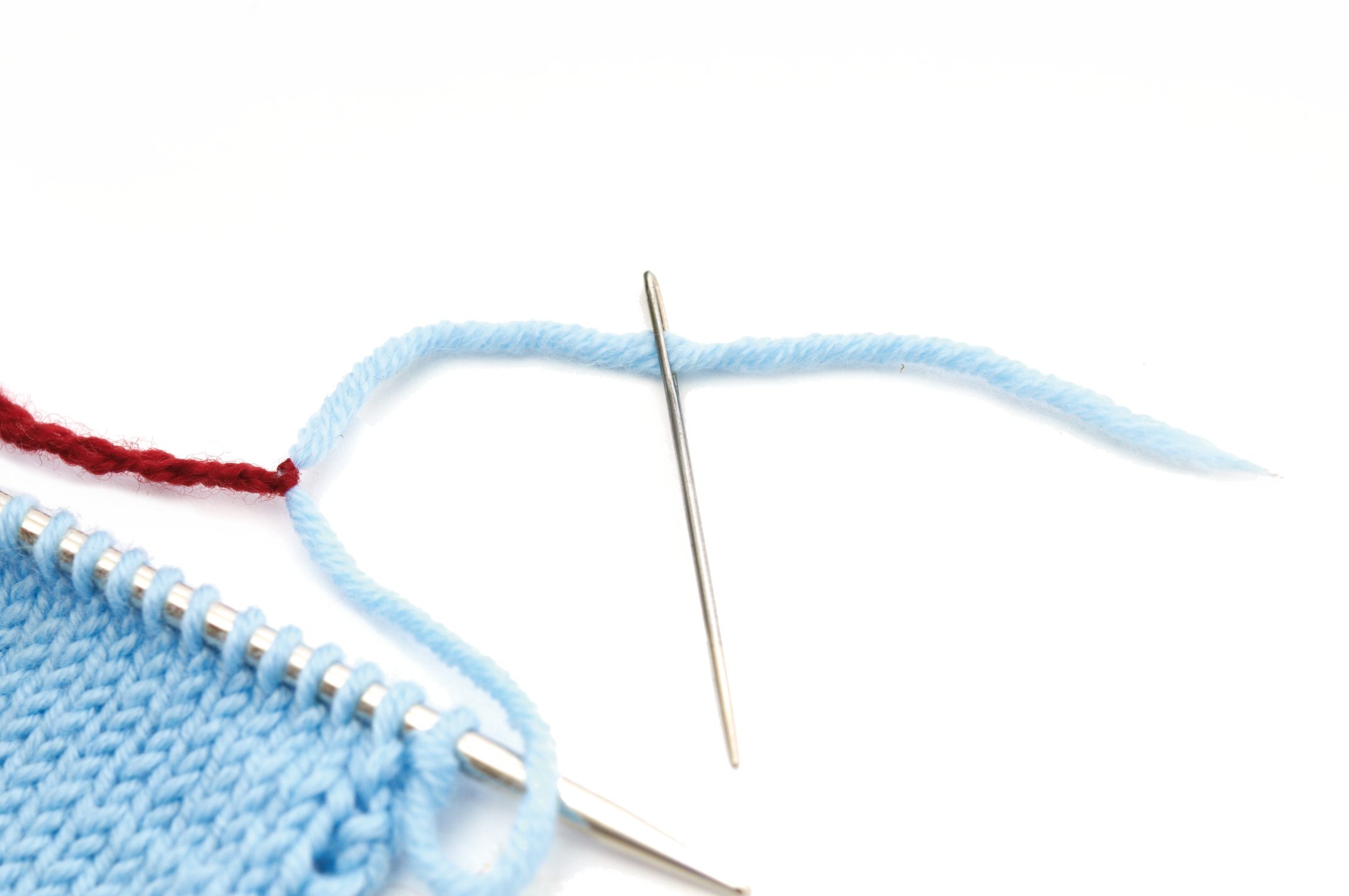 Hellblaues Strickprojekt mit silberner Nadel, Kontrastgarn in Rot. Handarbeit, diy, modisch.