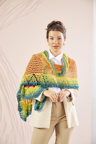Buntes, handgemachtes Häkelmuster in Regenbogenfarben, lässig über beigem Blazer getragen. DIY-Chic.
