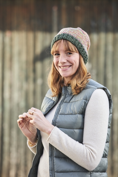 Modische Strickmütze in Grün-Rosa, graue Weste, warme Farbtöne, handgemachte Details, gemütlich.