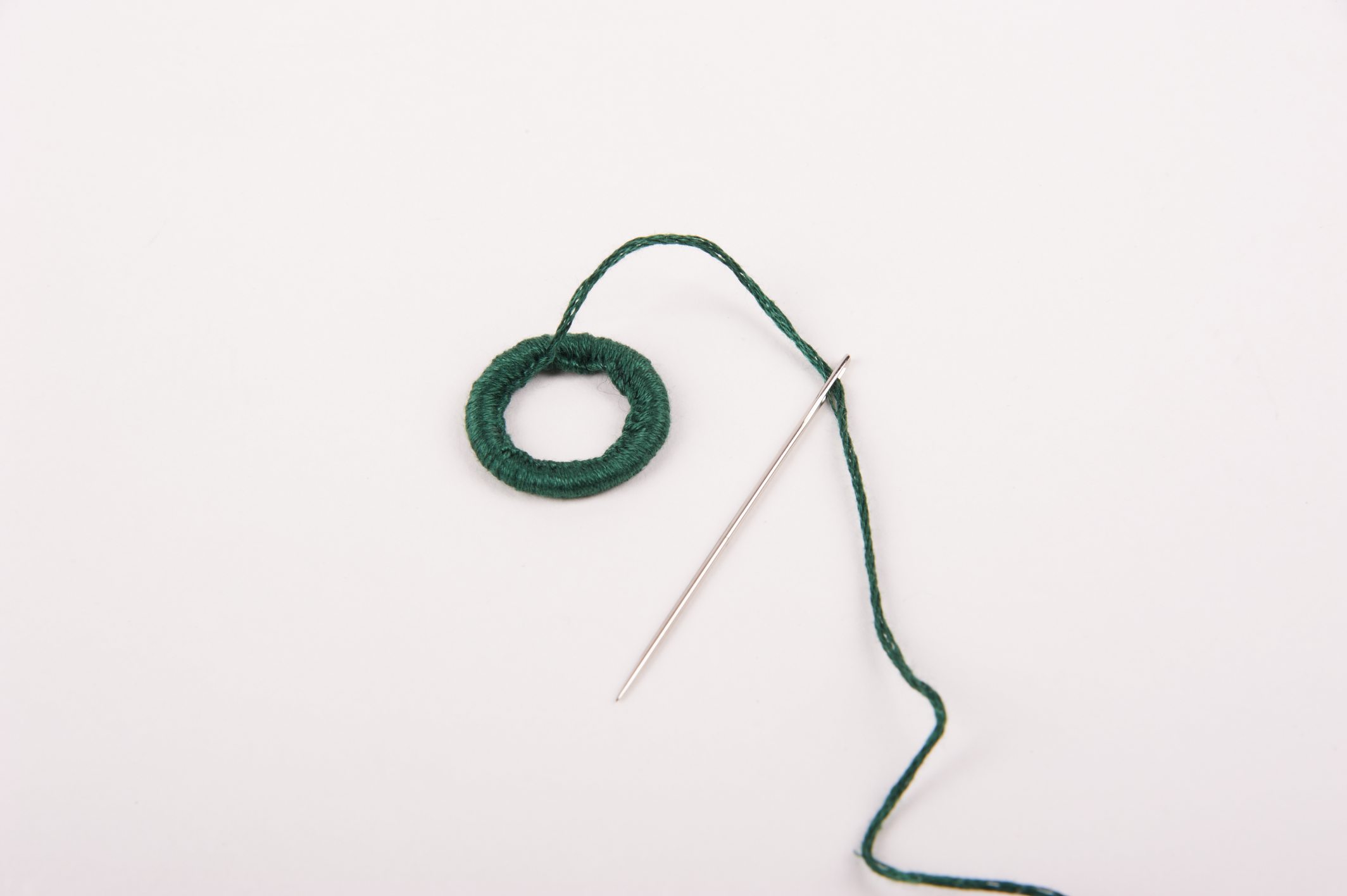 Grüner Garnring mit Nadel. Handarbeit betont durch den DIY-Charakter. Einfache, aber modische Detailarbeit.