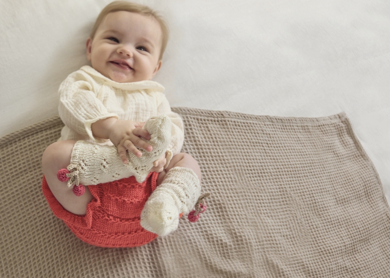Modisches Babyoutfit: creme Strickpullover, handgemachte rote Hose, kreative DIY-Strickmuster.