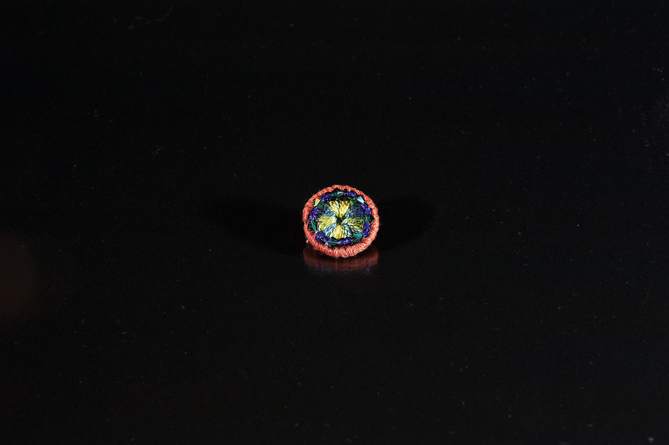 Handgemachter Knopf mit farbenfrohem Muster, runder Schnitt, DIY-Look. Lebendige Blau- und Goldtöne umrahmt von Rot.