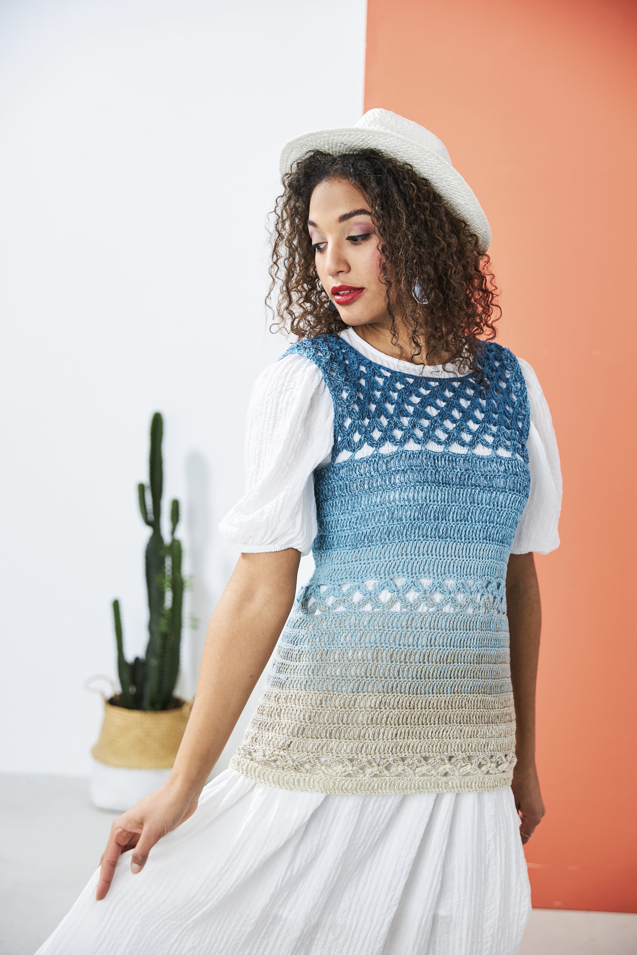 Gehäkeltes Top in Blau- und Beigetönen, mit weißem Puffärmelkleid und Strohhut kombiniert. Handarbeit, DIY.