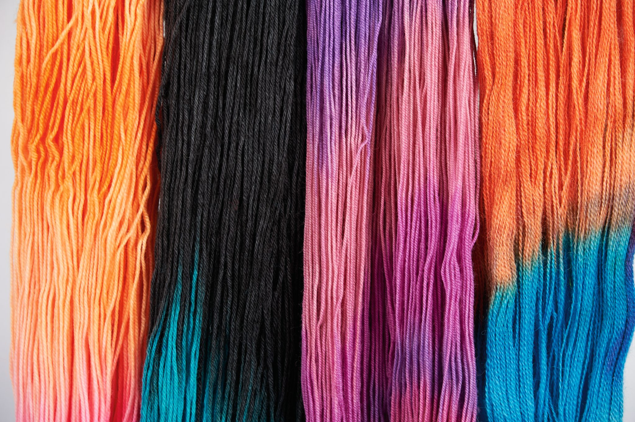 Handgefärbte Wolle in lebendigen Tönen: Orange, Schwarz, Violett, Blau. Kreative DIY-Handarbeit.