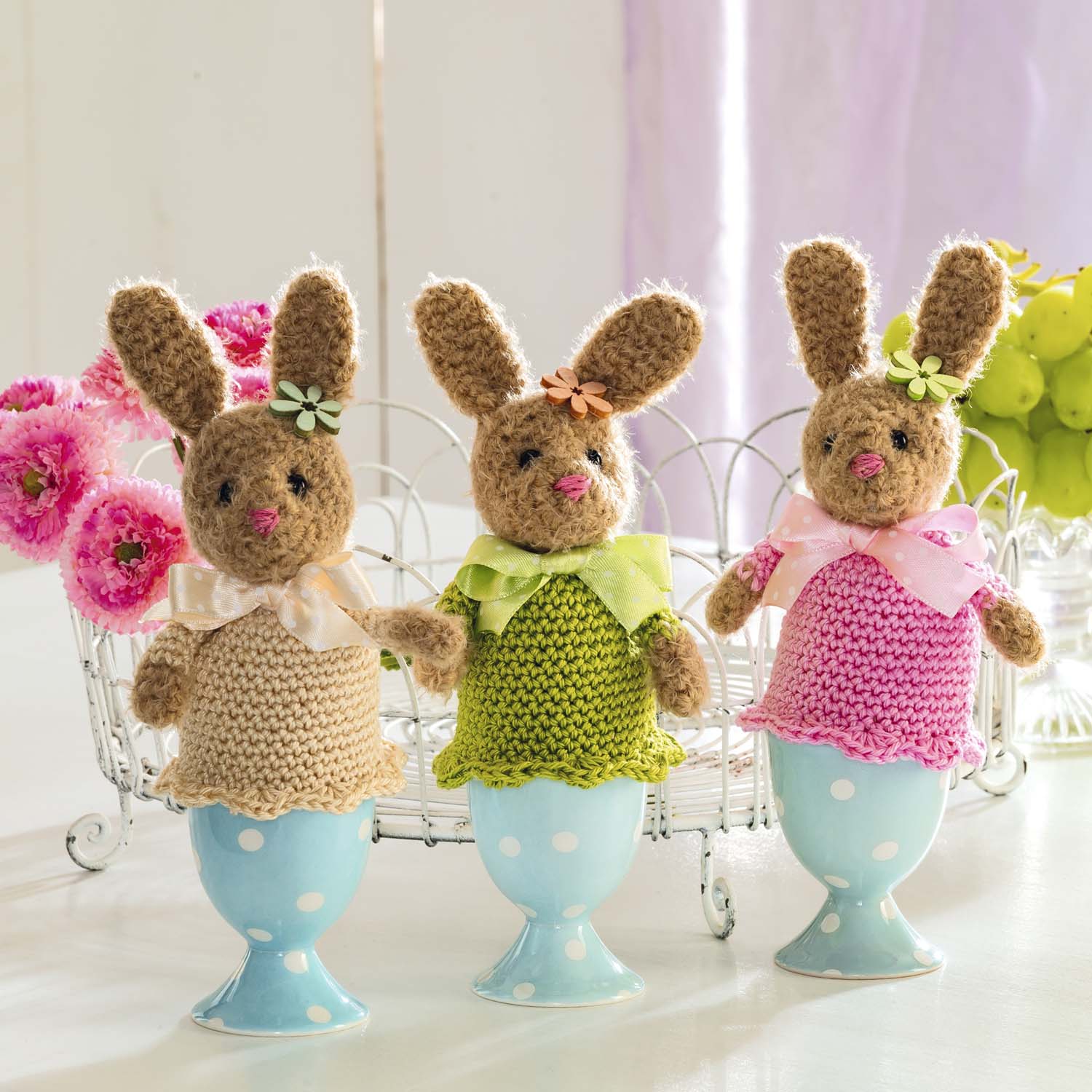 DIY Häkelhasen, modisch und handgemacht, bunte Kleider in Beige, Grün, Pink. Jedes mit Blumendetail und Schleife.