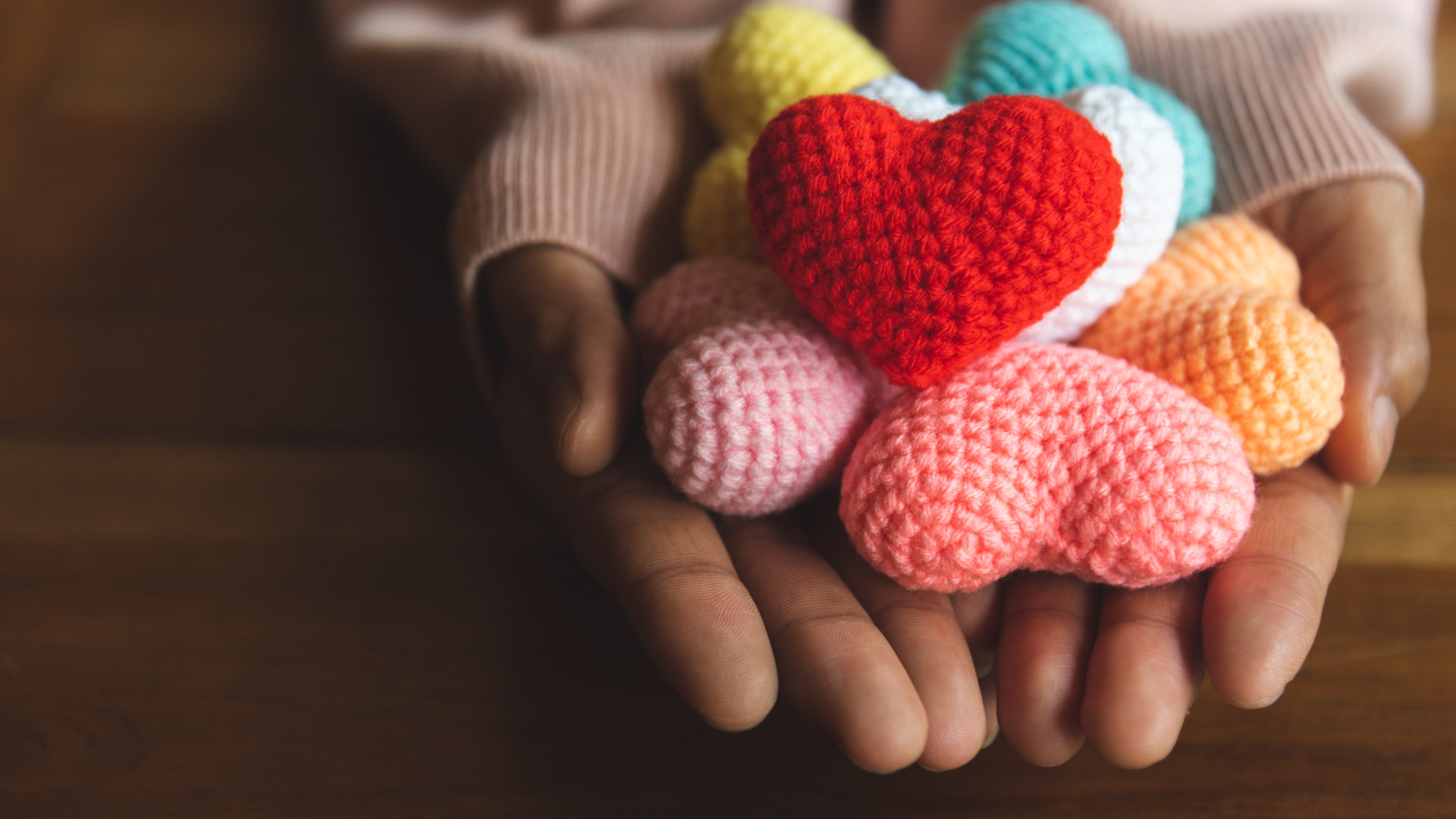 Handgemachte, bunte Häkelherzen, kunstvoll in den Händen, diverse Farben, kreative Handarbeit, DIY.