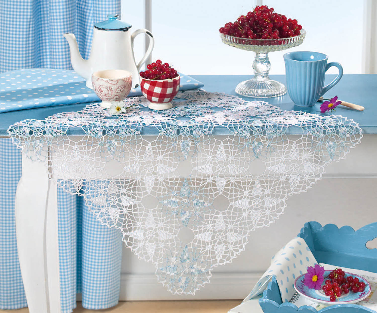 Weiße, gehäkelte Tischdecke mit filigranem Muster über blau-gepunktetem Stoff. DIY, stilvoll, nostalgisch.