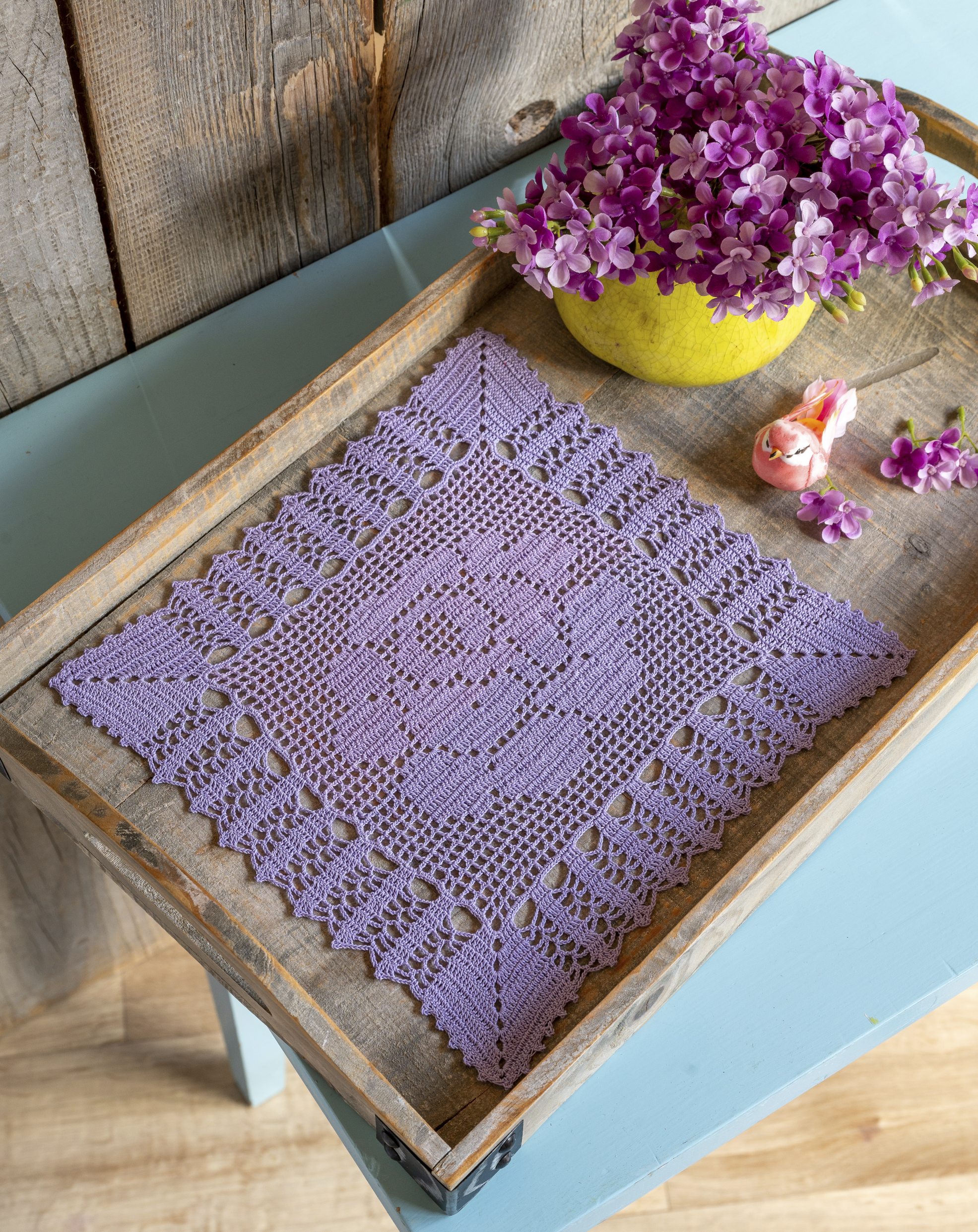 Quadratische, handgemachte häkeldecke in lila mit floralen und geometrischen Mustern im stilvollen Design.