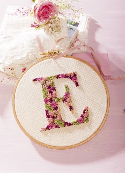 Buntes, handgemachtes Stickmuster im Holzrahmen mit floralen Akzenten, verziert mit kreativen DIY-Elementen.