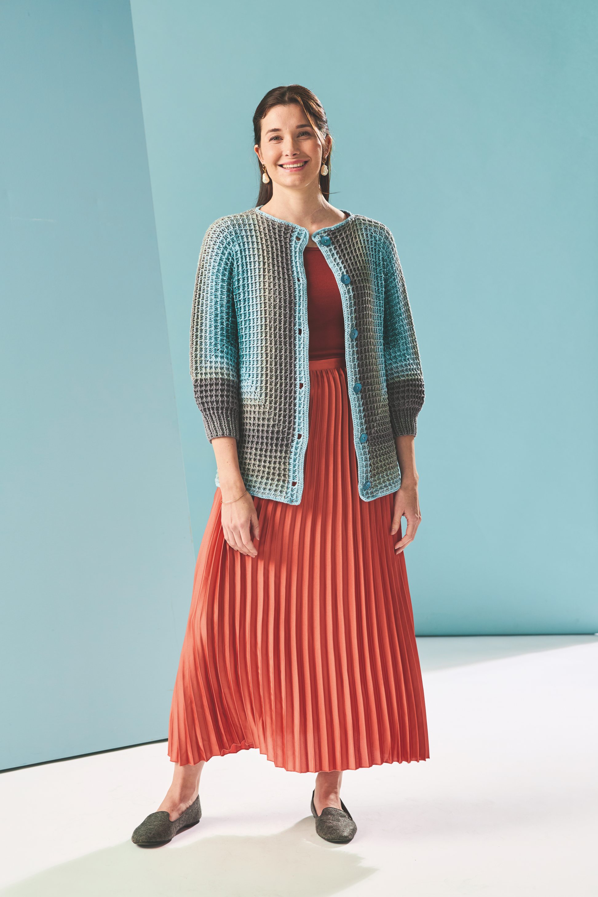 Farbenfrohe, handgemachte Strickjacke in Blau-Grau, kombiniert mit einem orange-roten Plissee-Rock.