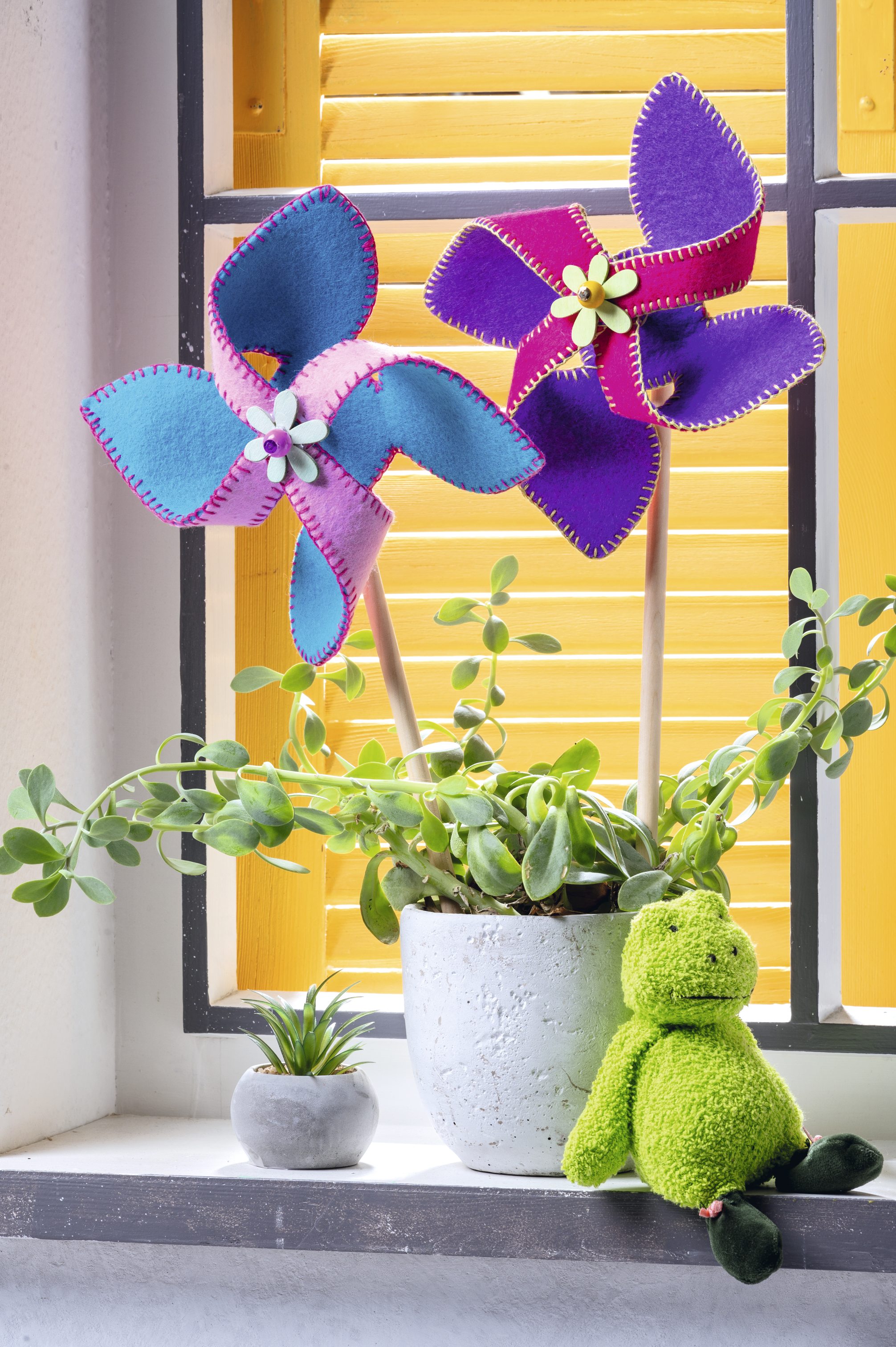 Bunte Filz-Windräder in Blau und Lila mit Ziernaht und Blumenakzent, handgemacht, diy-Charme.