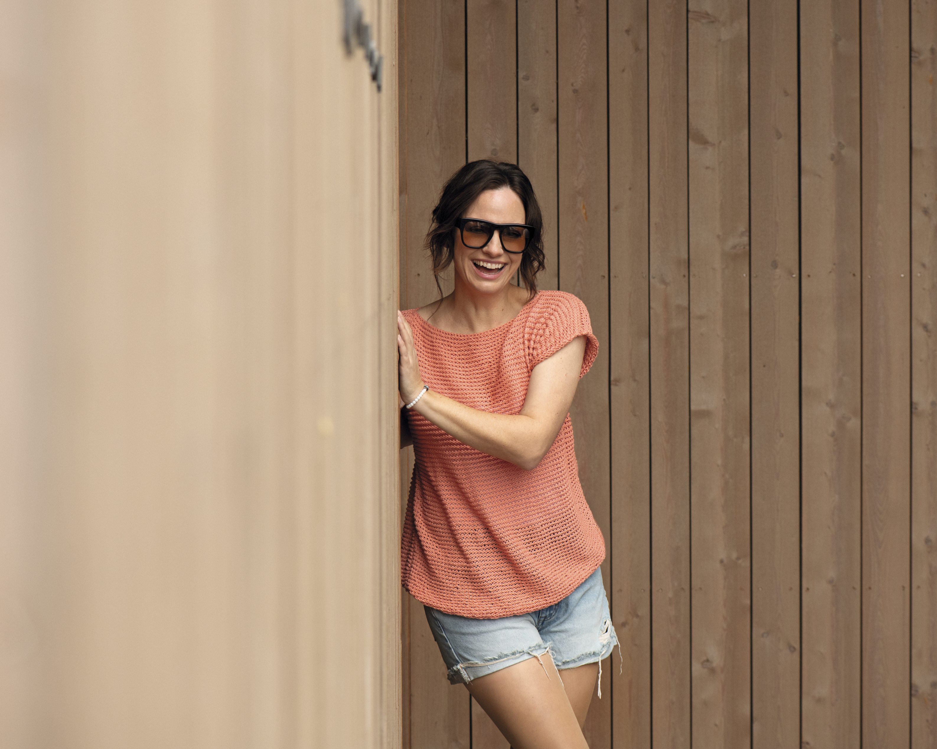 Modisches, gehäkeltes Oberteil in Koralle mit lockerer Passform; kombiniert mit schlichten Denim-Shorts.