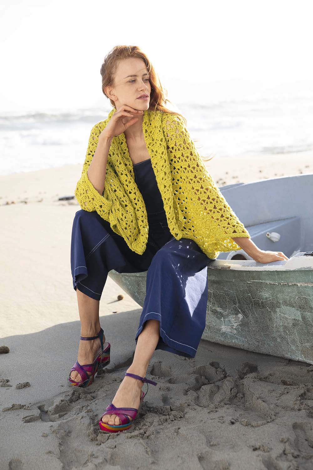 Gelbes gestricktes Cape, modisch, handgemacht. Dunkle, weite Hose, farbenfrohe Sandalen. Stilvoll und kreativ.