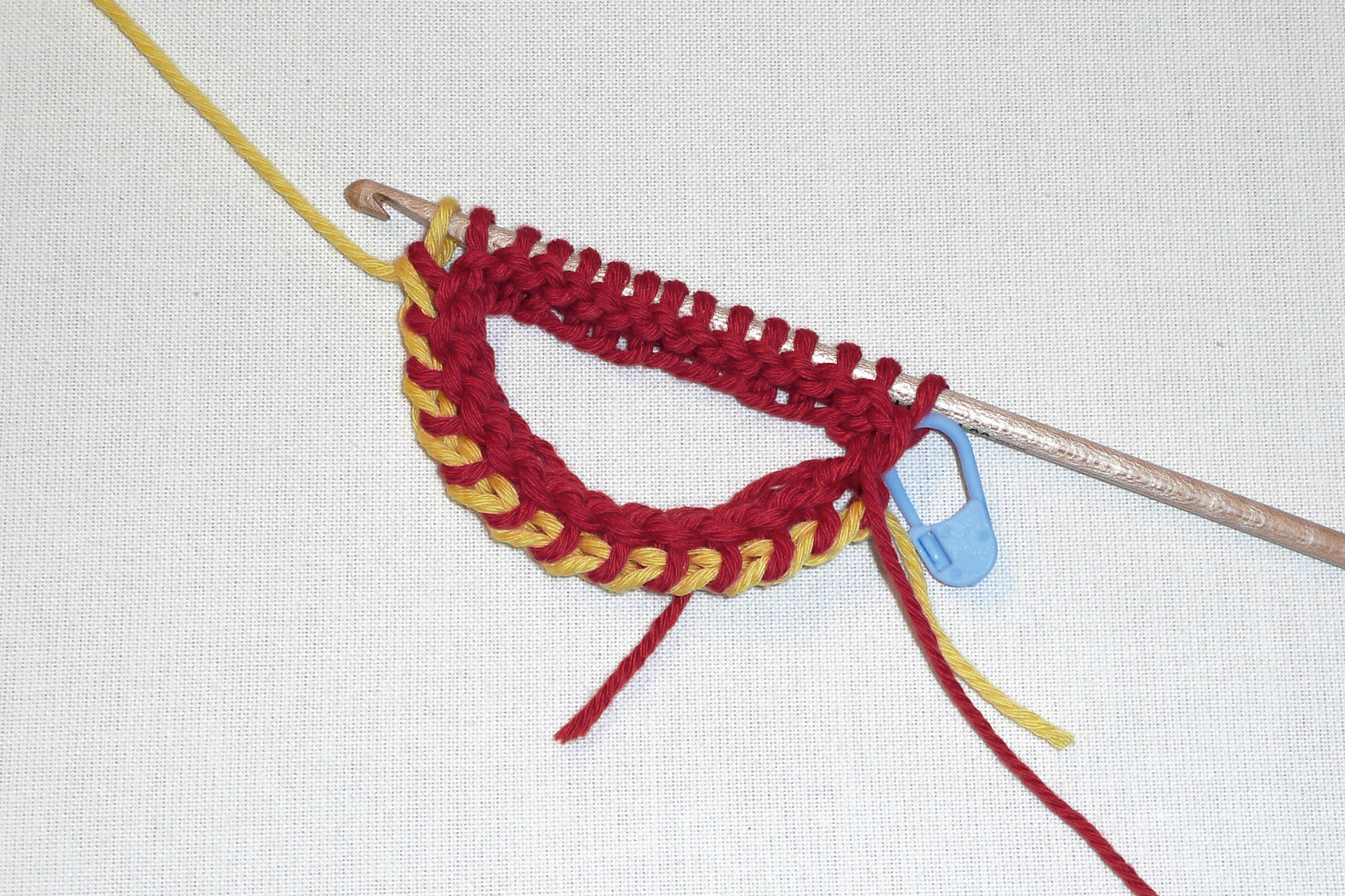 Handgemachte rot-gelbe Häkelarbeit mit blauem Marker. Lebendige Farben, DIY-Charme, modisch.