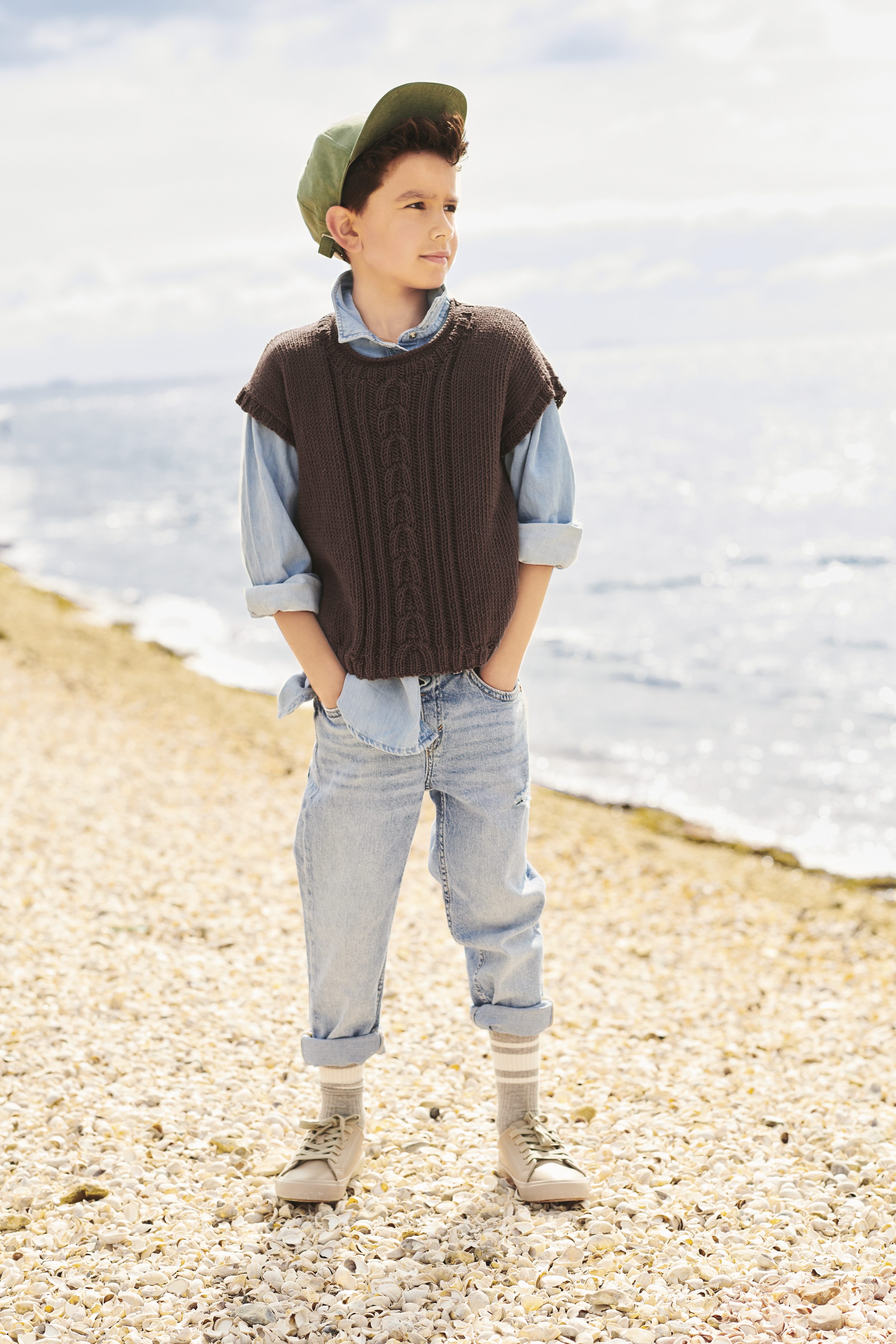 Braune Strickweste über hellblauem Hemd, hochgekrempelte Jeans. Legerer, modischer Stil.