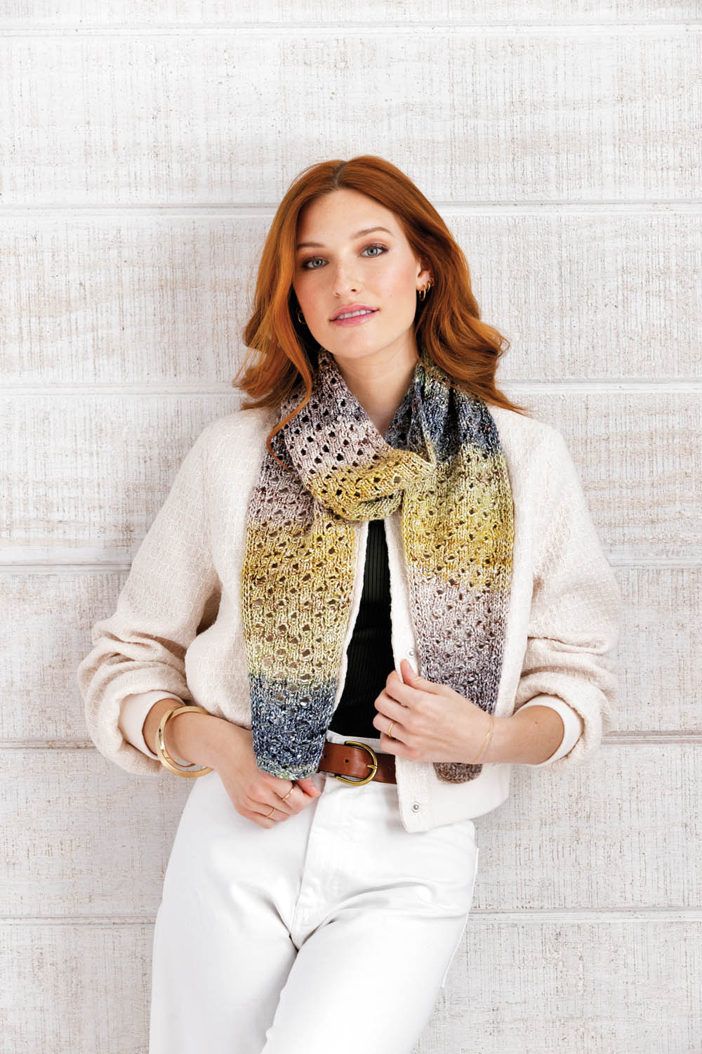 Modischer Strickschal in Gelb- und Grautönen, strukturierte Jacke, weiße Hose; zeitloser und detailreicher Look.