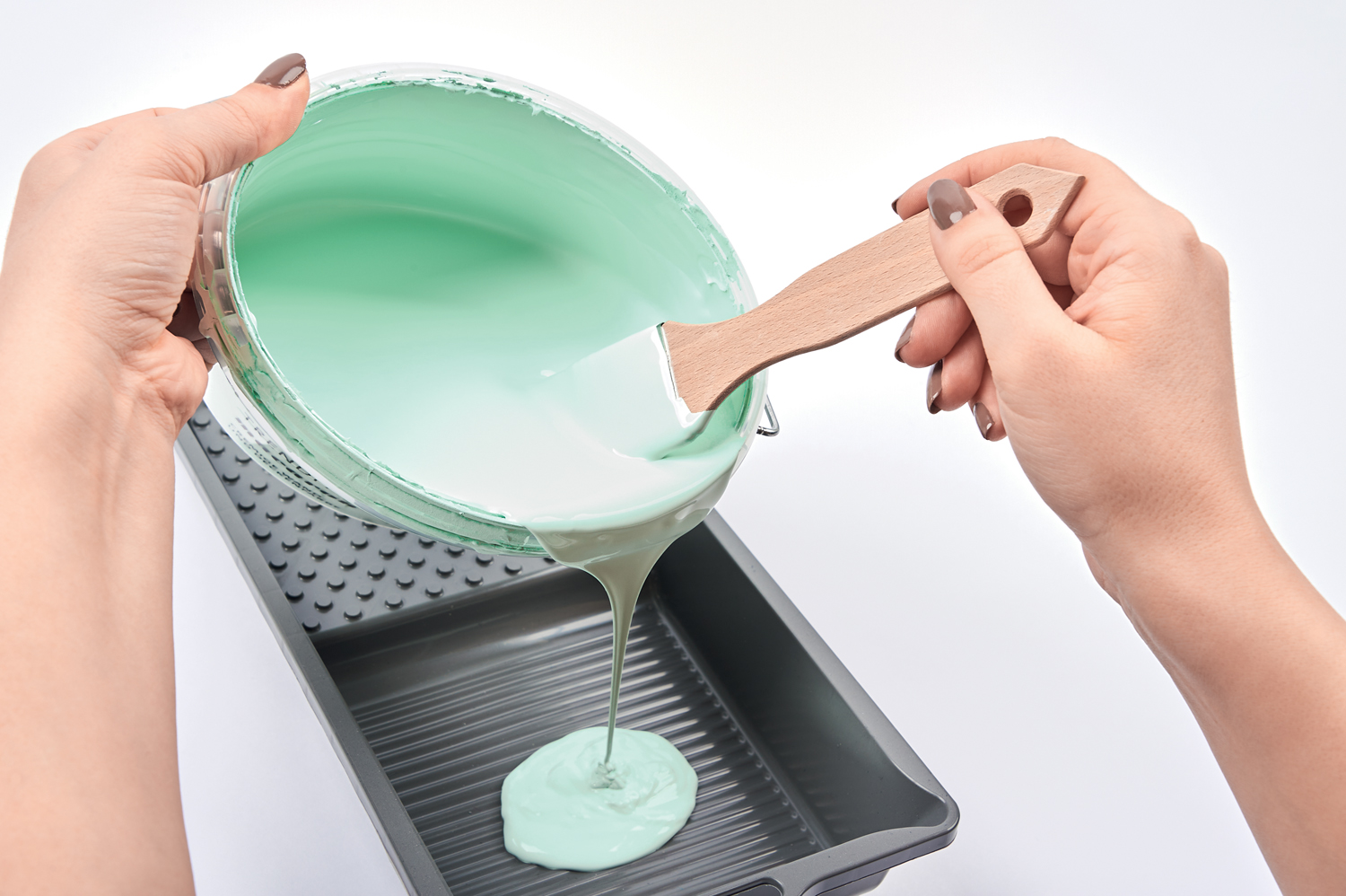 Person gießt mintgrüne Farbe von Schale in Farbwanne, modernes Malprojekt, DIY, einfache Handarbeit.