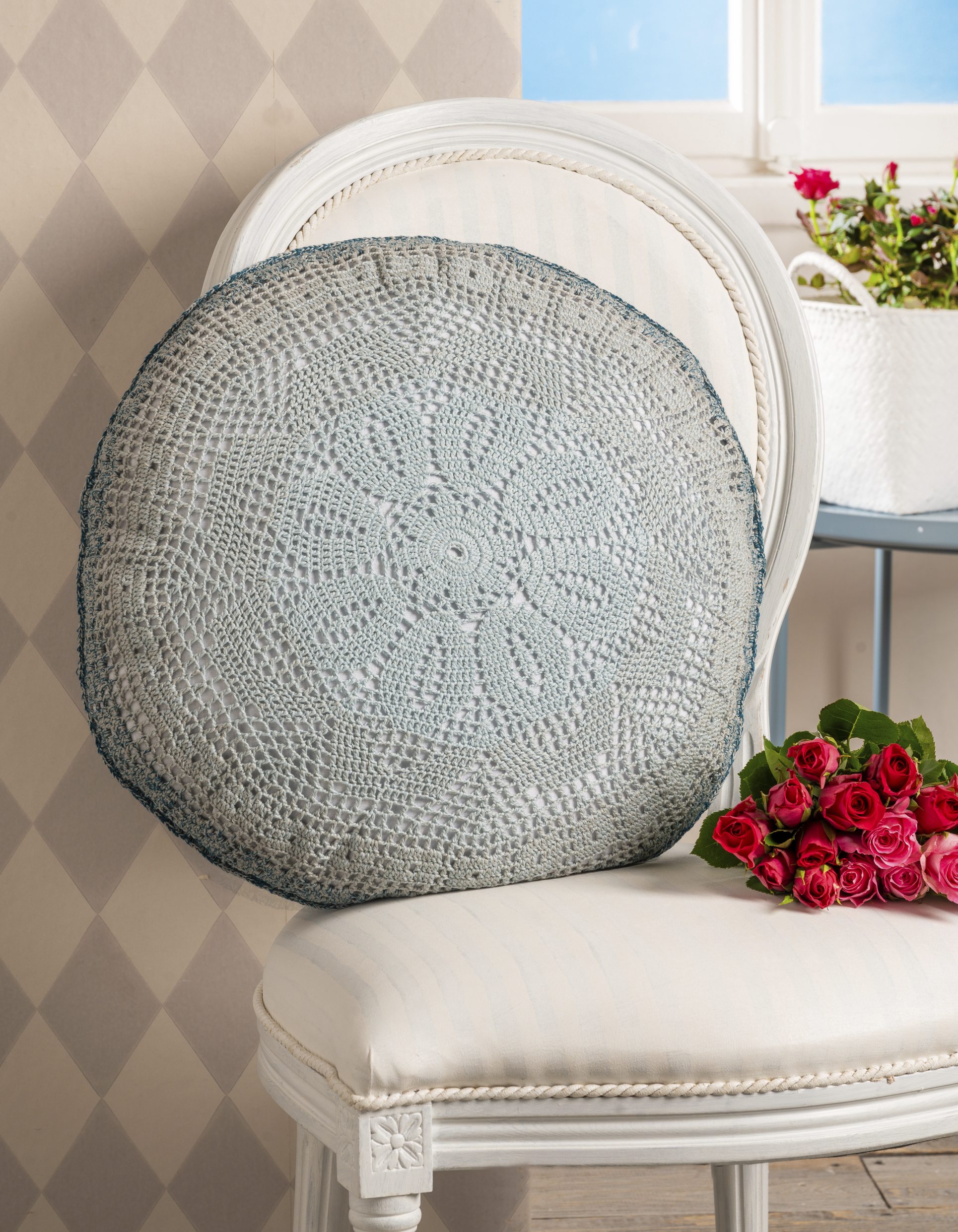 Rundes, hellgraues Kissen mit gehäkeltem Blumenmuster, modisch und handgemacht. DIY-Stil.