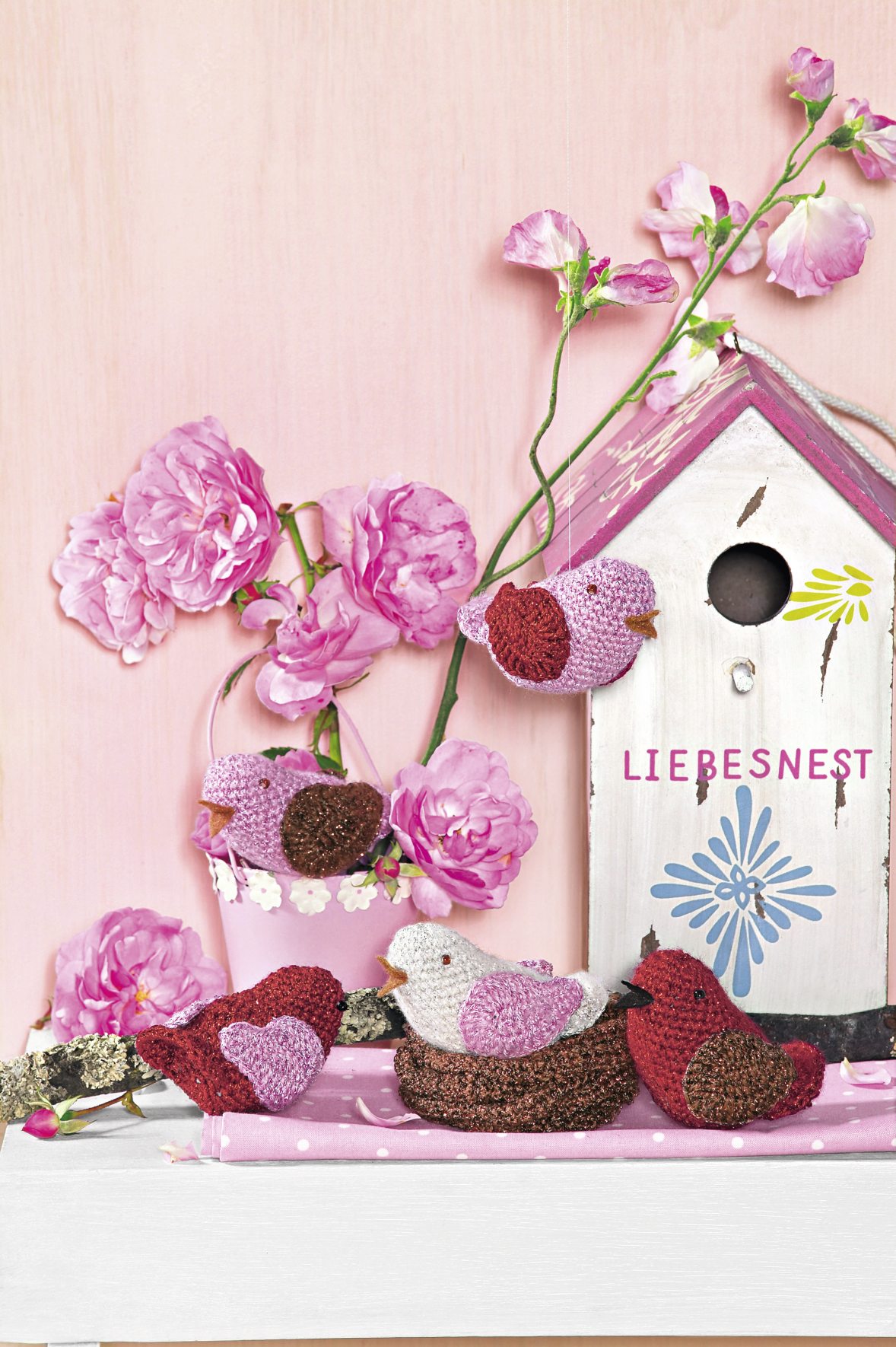 Bunte, gehäkelte Vögel vor rosa Haus. Kreativ, handgemacht, modisches Muster. DIY-Charme.
