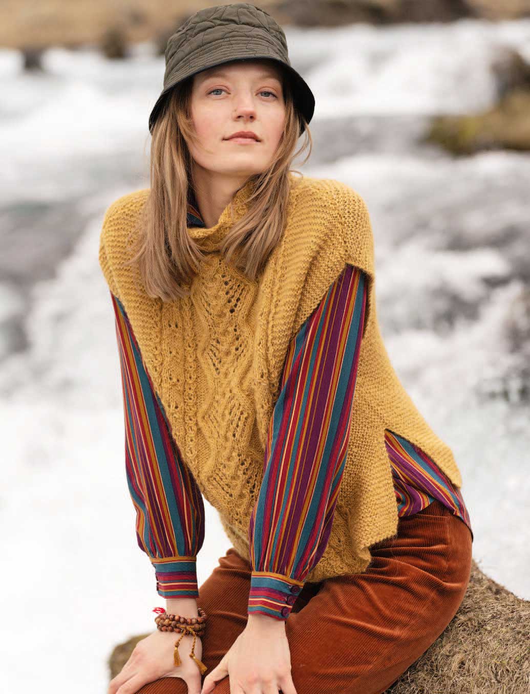 Handgestrickter, senfgelber Pullover mit Zopfmuster, gestreifte Ärmel, brauner Hut. Modern, selbstgemacht, vintage.