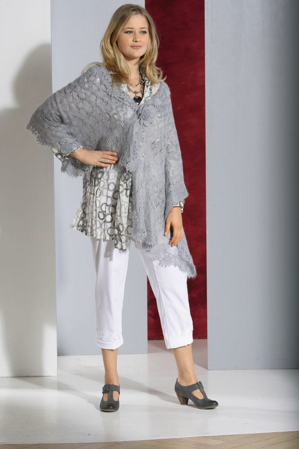 Modischer grauer Poncho, handgemachte Optik, kombiniert mit geometrischem Musterkleid, weiße Hosen, passende Schuhe.