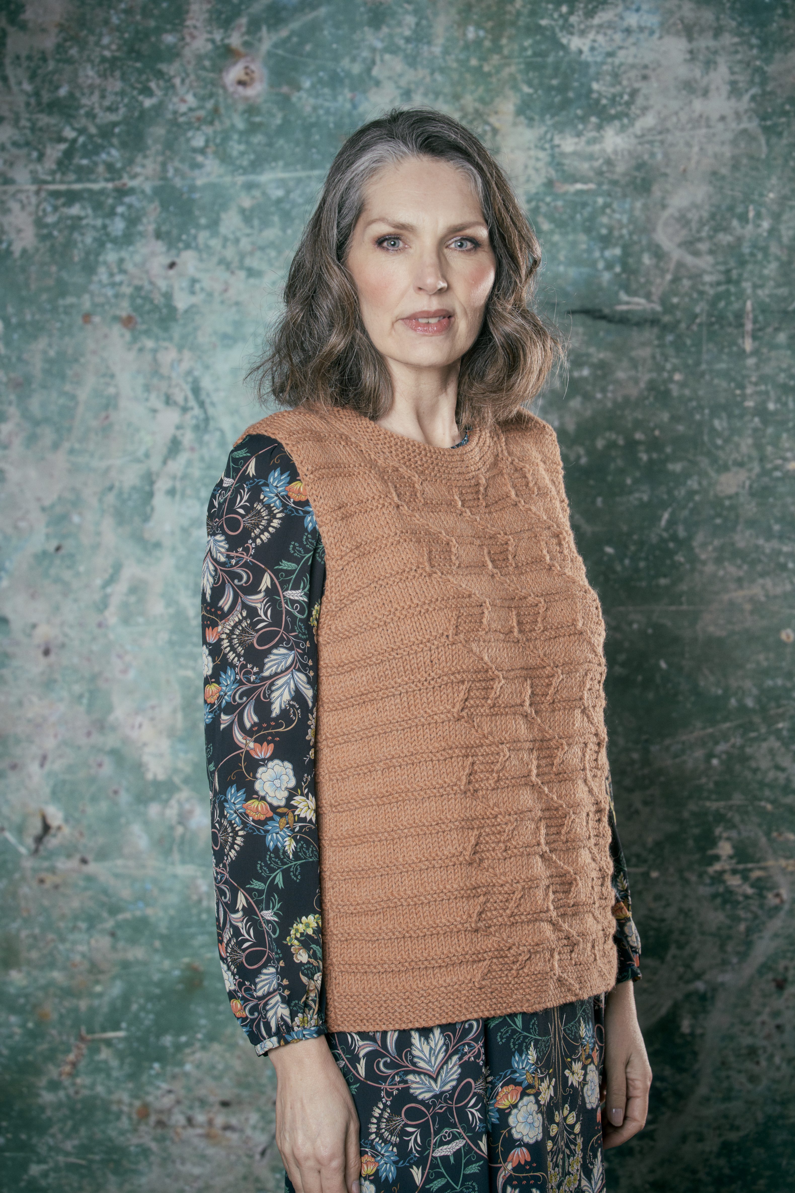 Modischer, handgemachter Pullover in Erdtönen über floralem Kleid mit langen Ärmeln.