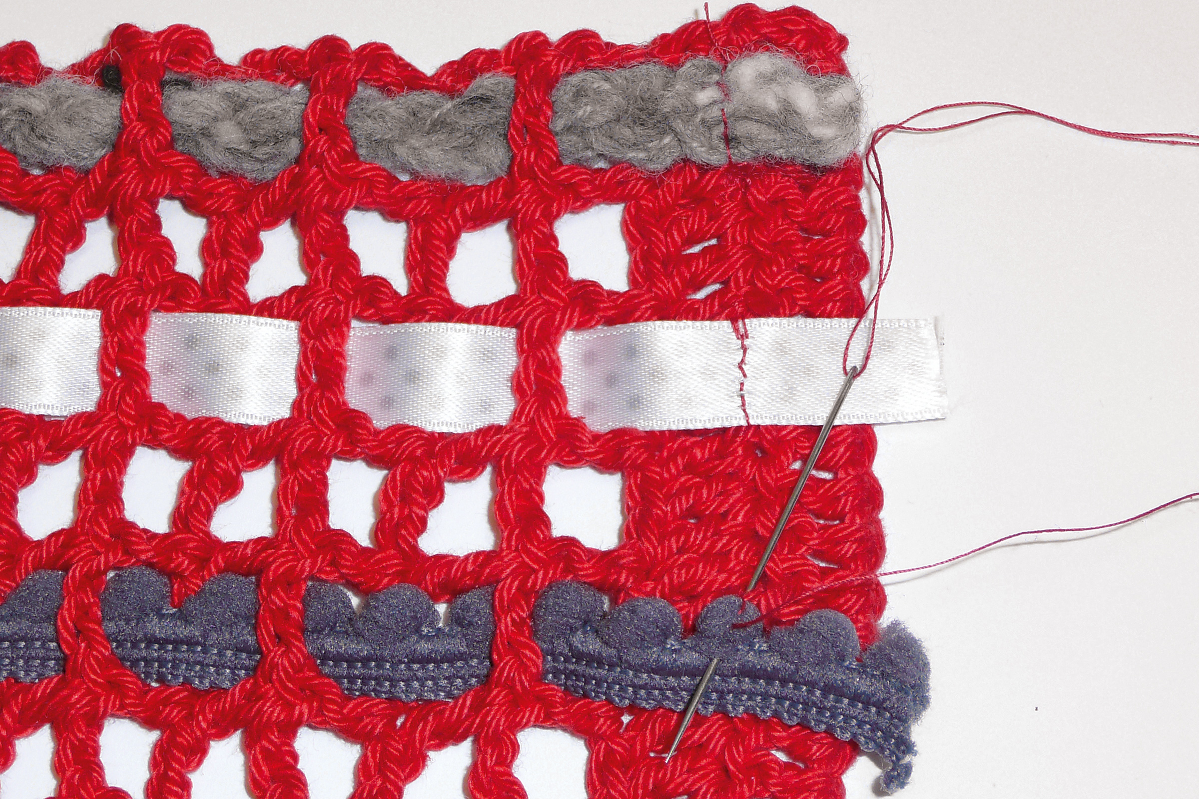 Leuchtend rotes, handgemachtes Häkelmuster mit grauen Akzenten und weißen Bändern, DIY-Charme.