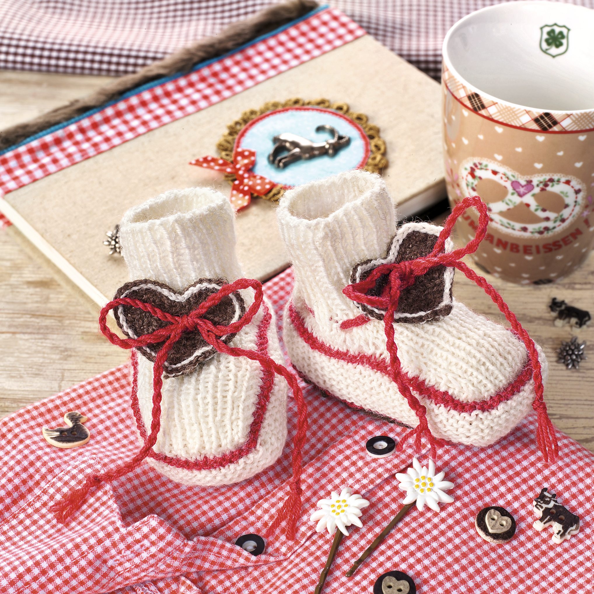 Handgemachte Baby-Booties, cremefarben mit roten Akzenten, dekorative Herzapplikationen. DIY-Stil, modisch.