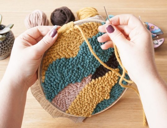 Bunte, selbstgemachte Stickerei mit Wolle; modernes Muster in Gelb, Blau und Rosa. DIY Handarbeit.
