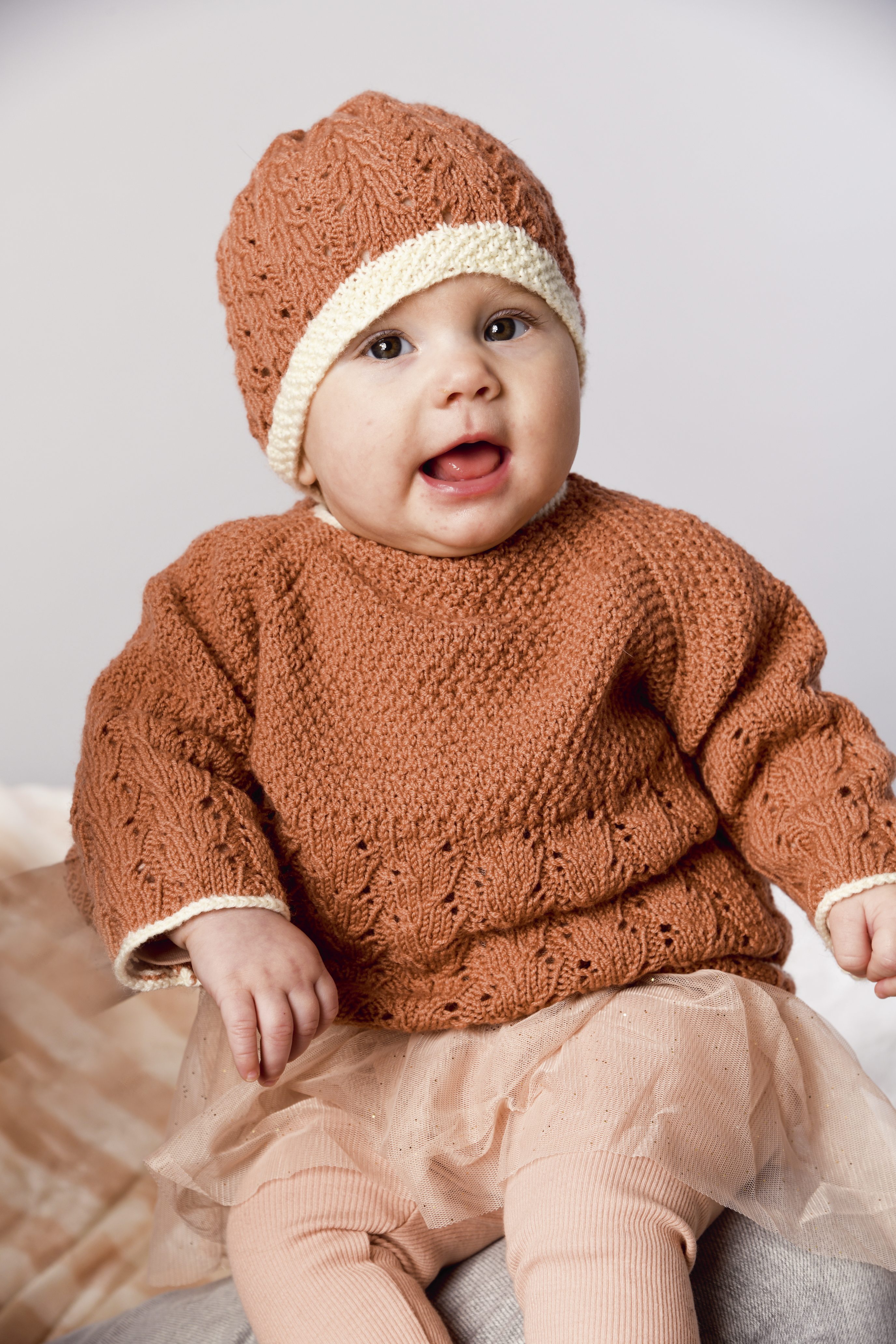 Modischer, handgestrickter Pullover mit passender Mütze in warmem Braun, kombiniert mit leichter Tüllröckchen.