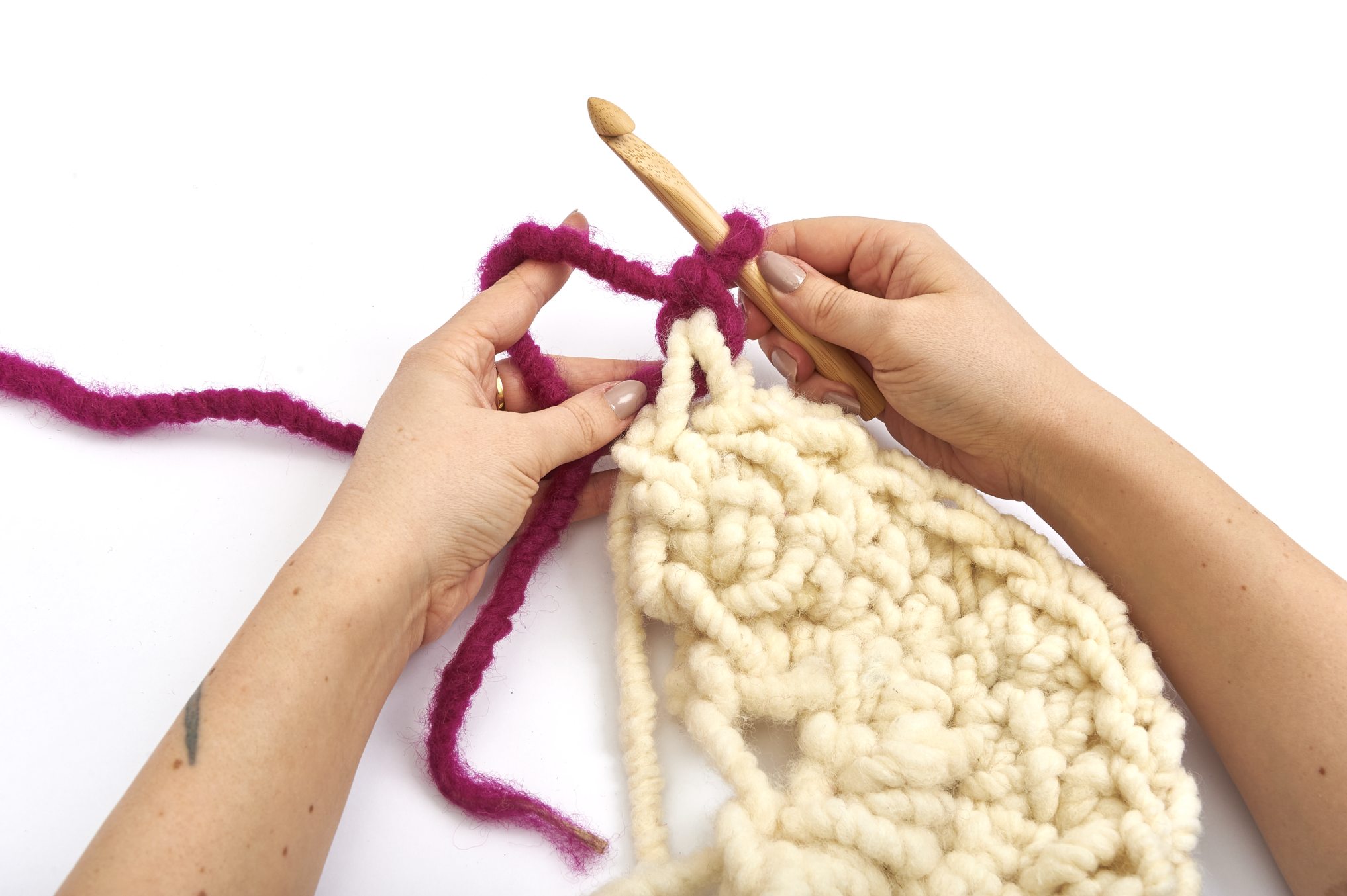 Handgemachtes Häkeln aus cremefarbener Wolle und lila Akzenten, strukturiertes Muster, DIY, handarbeit.