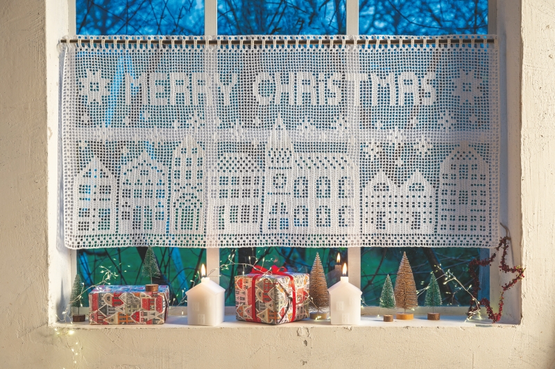Weißer, handgemachter Häkelvorhang mit 'Merry Christmas', dekorativen Mustern und winterlichem Häuserdesign.