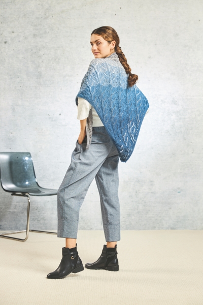 Ein handgemachter, blau-grauer Strickschal, kombiniert mit modischen, grauen Hosen und schwarzen Stiefeln.