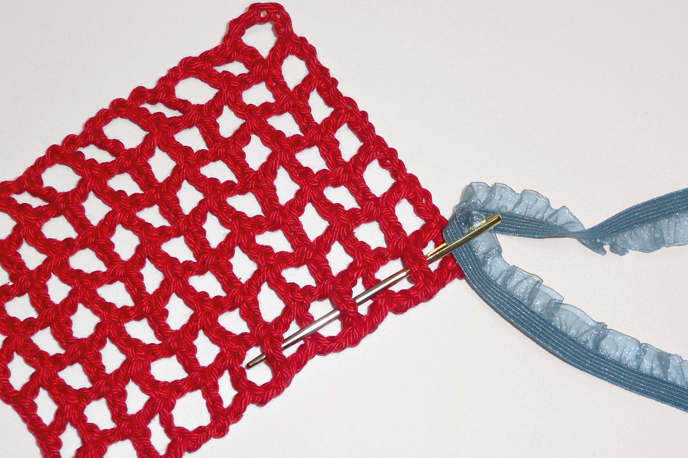 Rotes gehäkeltes Netz, handgemacht, mit grobem Muster. Akzentuiert durch blaues Band. DIY-Charme.