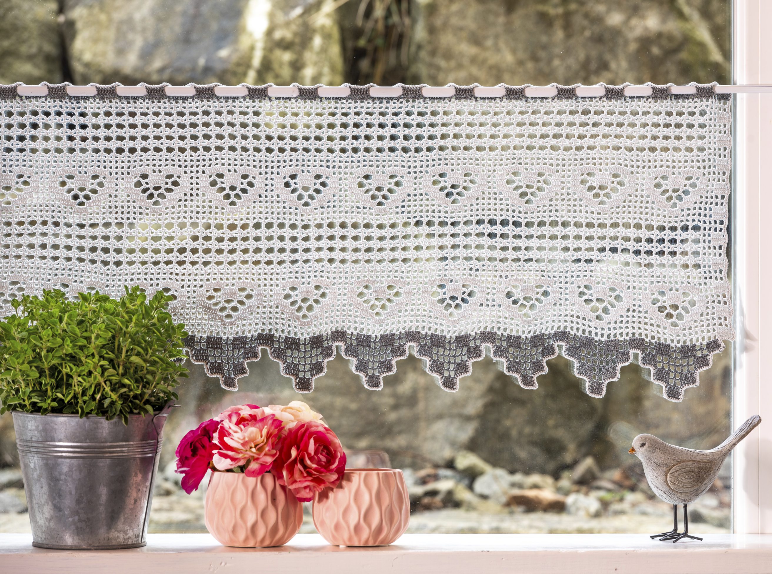 Weiße, selbstgemachte Häkelgardine mit Herzmuster und dekorativen Kanten. Romantische Handarbeit und DIY-Charme.