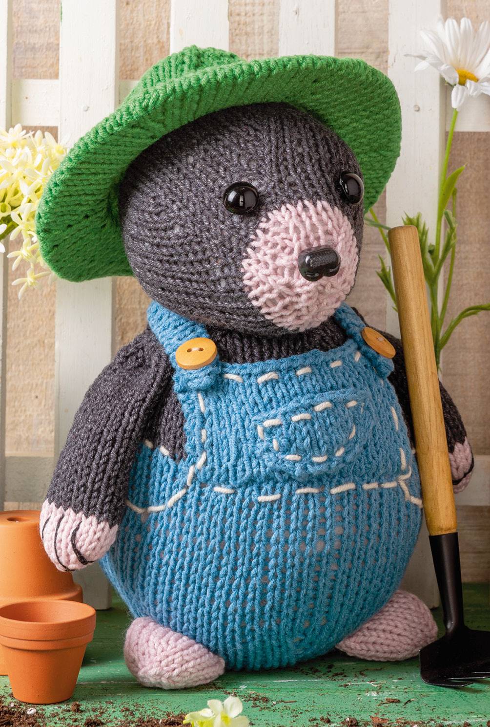 Selbstgemachter Maulwurf in blauer Latzhose, grünem Hut, gestrickt mit detailreichem Muster und Knopfdetails.