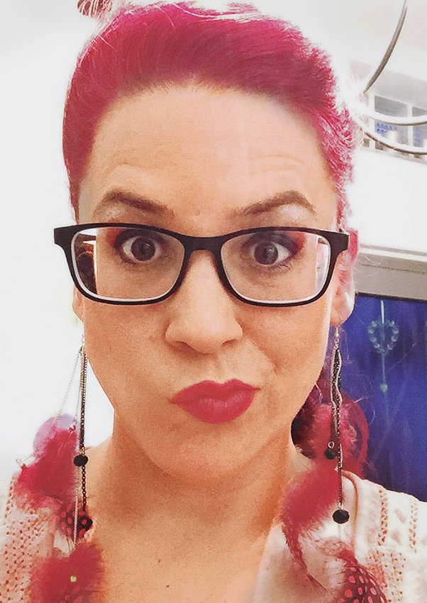 Leuchtend pinke Haare, lange DIY-Ohrringe, Brille. Modisches Statement mit kräftigen Farben.