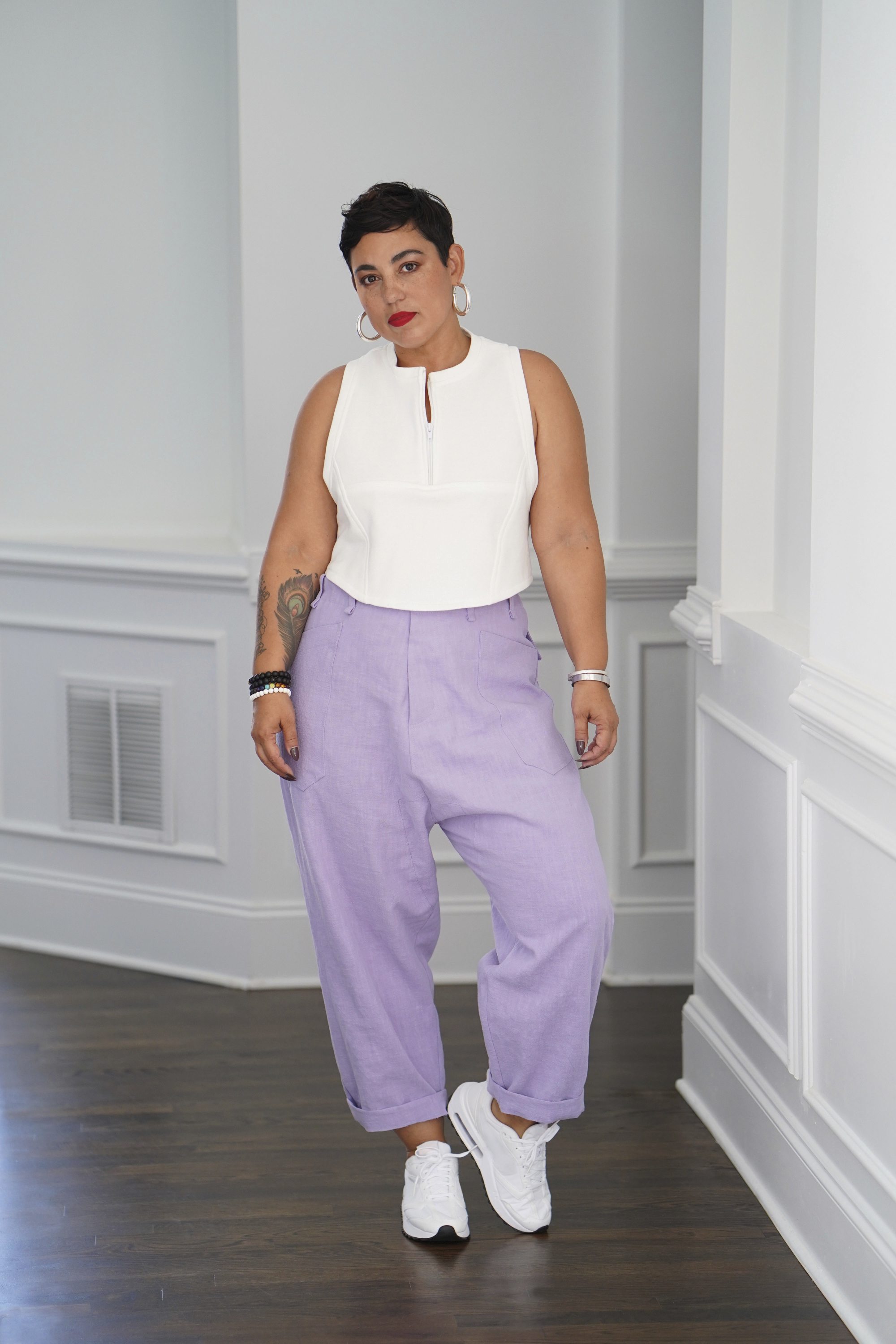 Weißes ärmelloses Top, fliederfarbene Hose, sportliche weiße Sneaker. Modischer und entspannter Look.