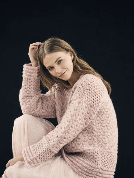 Handgemachter rosa Strickpullover mit Zopfmuster; kombiniert mit zartem, transparentem Rock. Stilvoll und gemütlich.