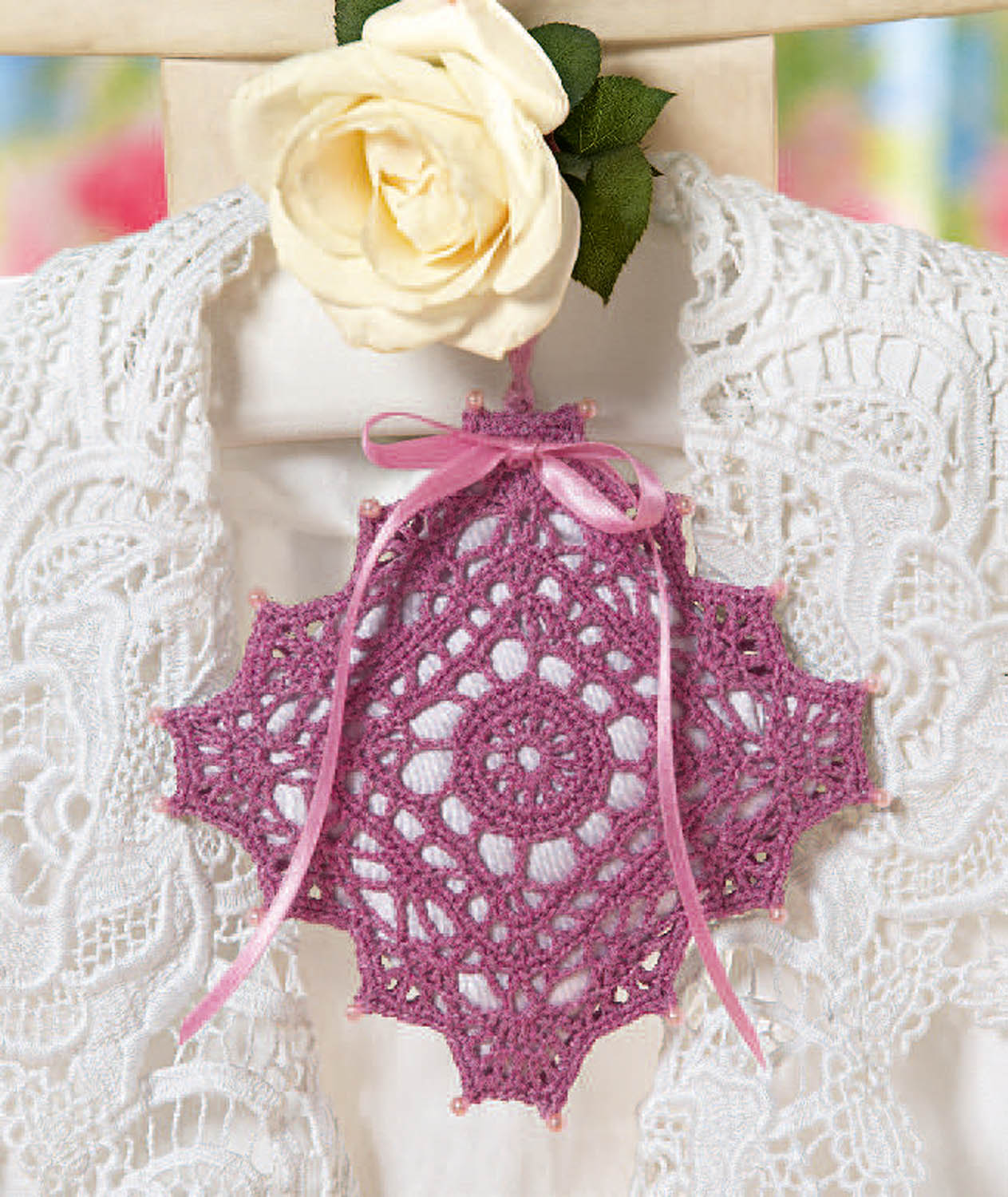 Rosa gehäkeltes Schmuckstück, filigran und handgemacht, verziert mit Schleife auf weißem Spitzenstoff.