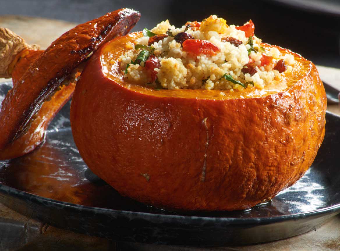 Leuchtend orange Kürbis, gefüllt mit buntem Couscous, stilvoll serviert. DIY-Kochkunst.