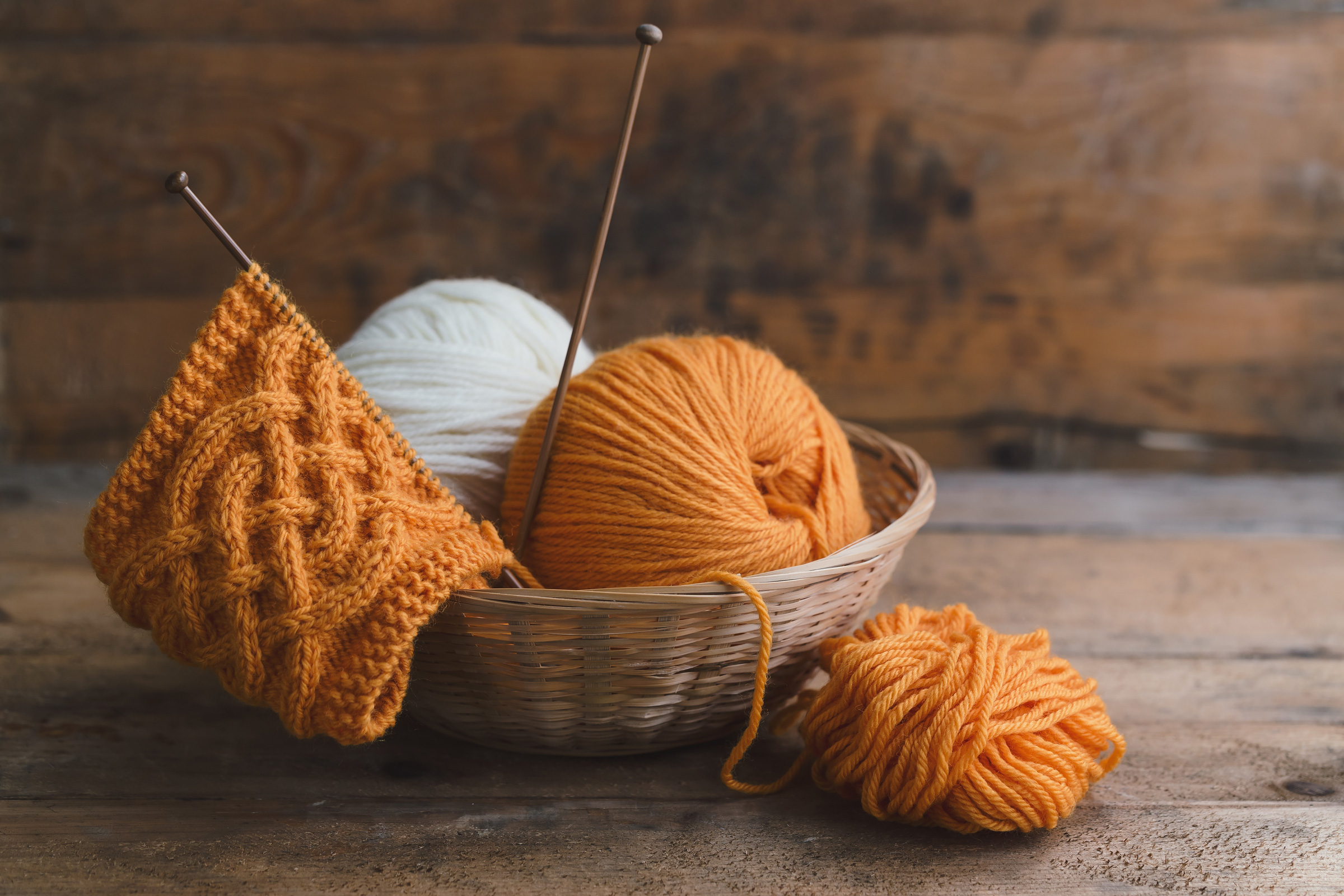 Orange handgestricktes Zopfmuster, Garn in Korb. Warm, kreativ, DIY-Strickprojekt.